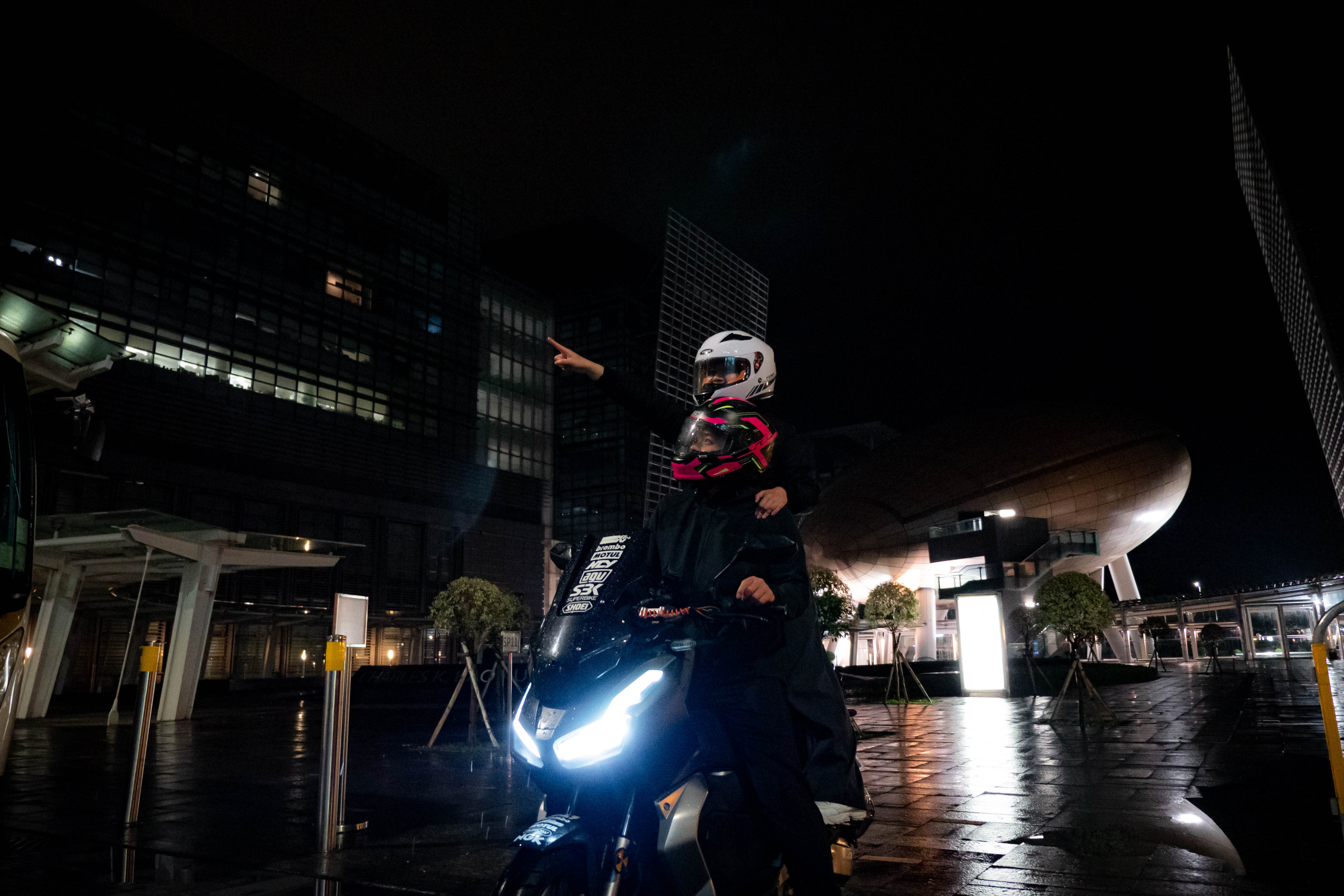 Motorcycle and riders in a wide night view of a Hong Kong plaza and towers
