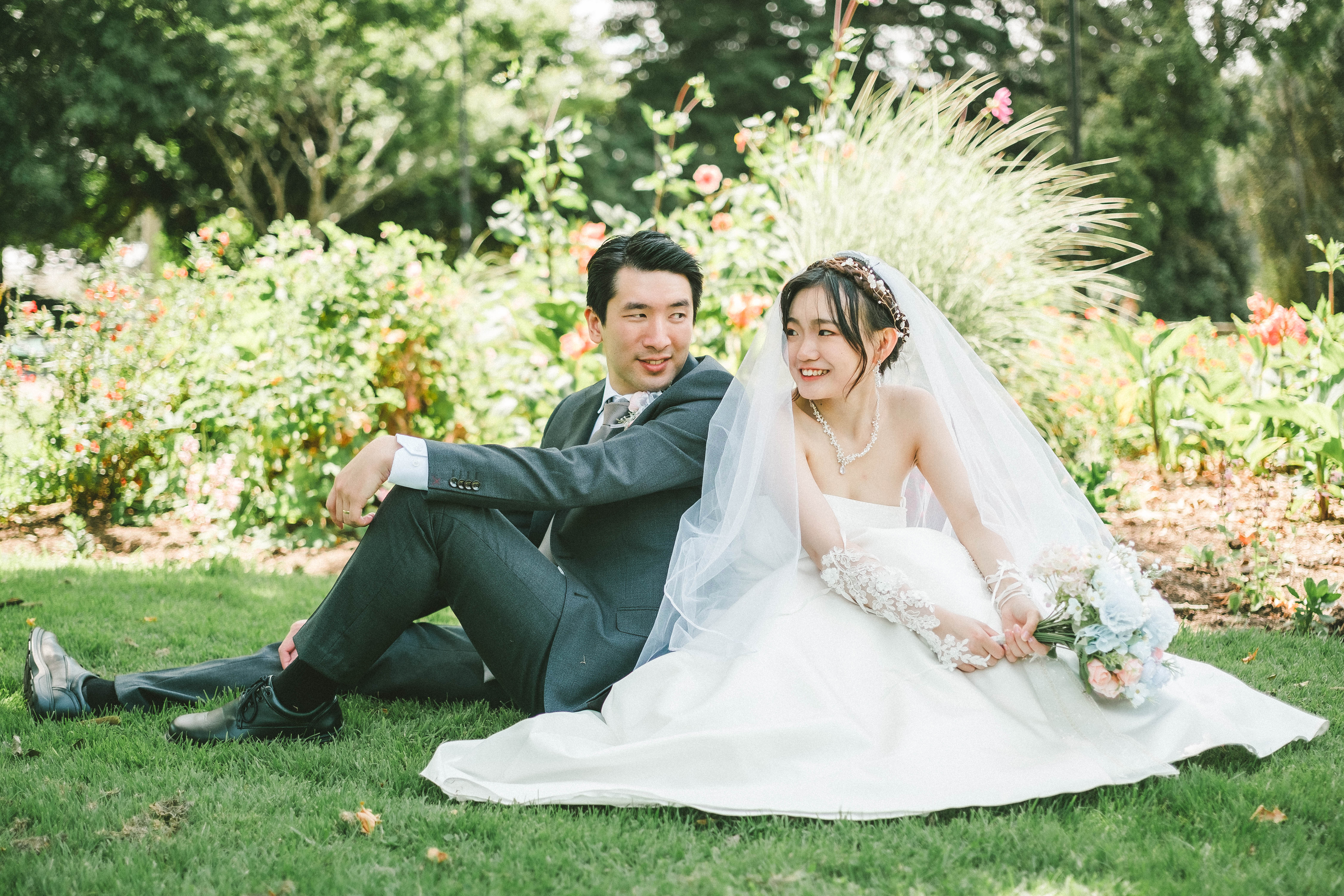 Hans and Chrystynn sitting on the lawn in front of flower beds, smiling at each other