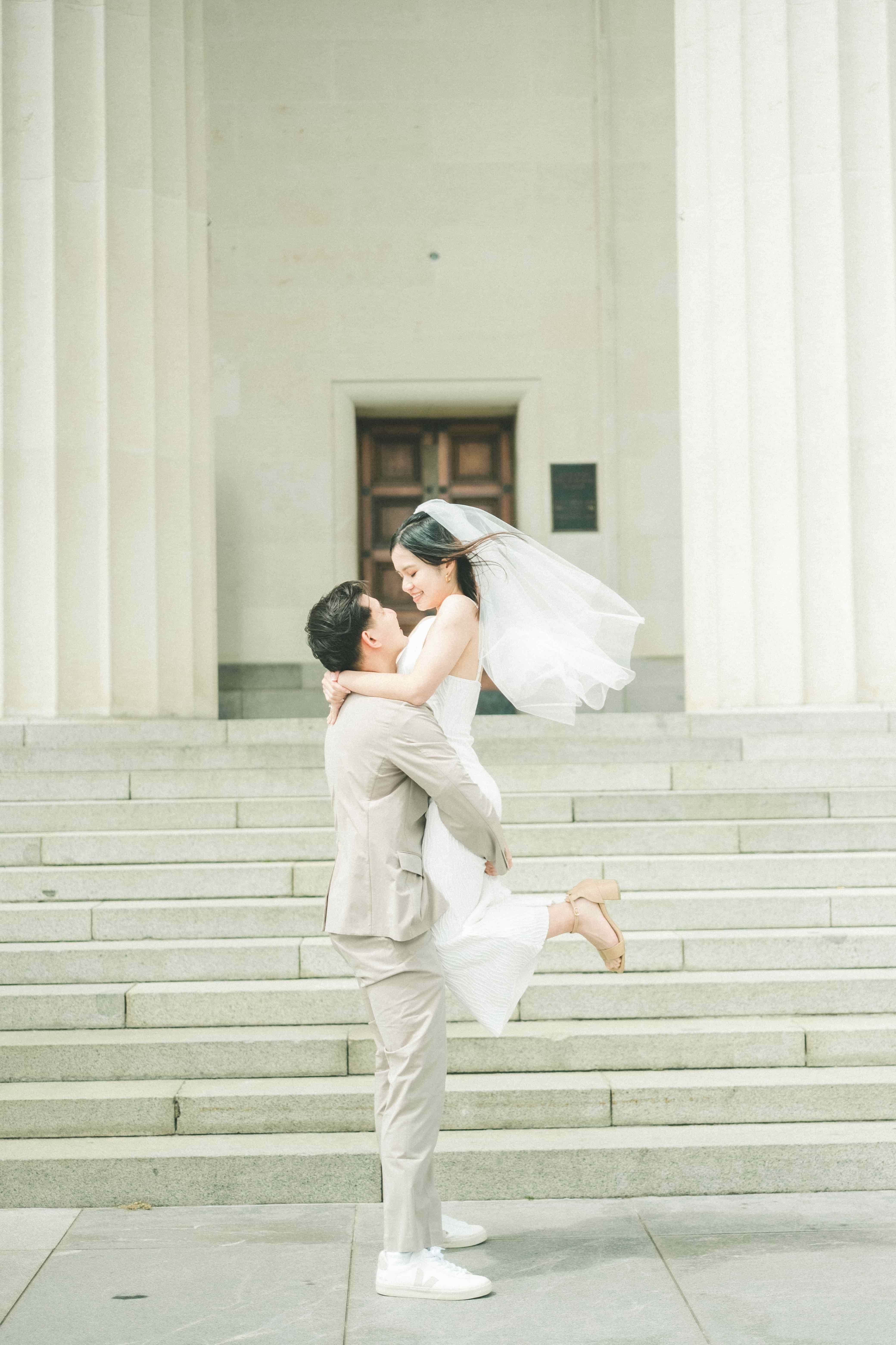 Nick lifting Suzen as her veil blows in the wind at the foot of grand stone steps