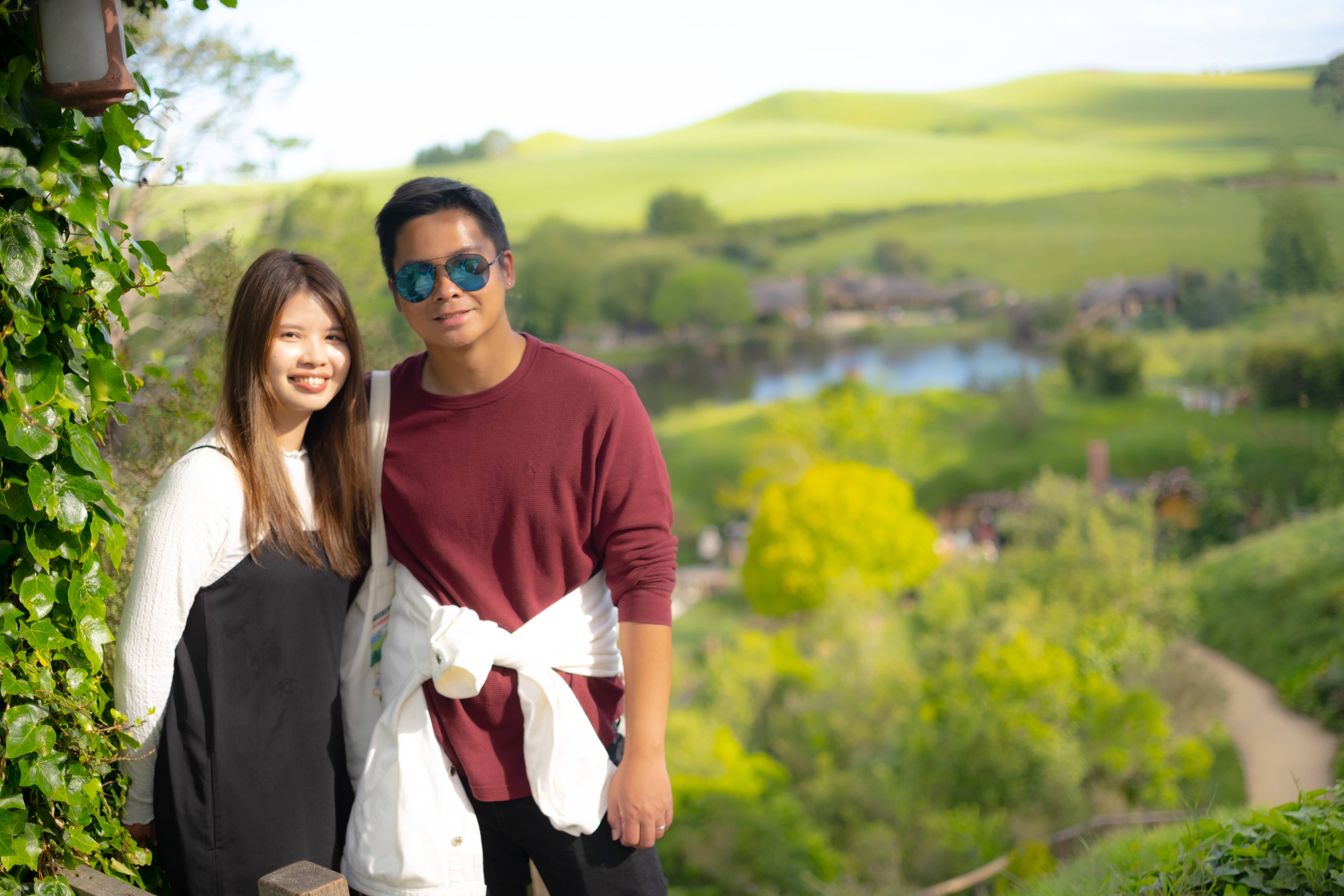 Julio and Kanis smiling on a hillside with green rolling farmland and a pond behind them