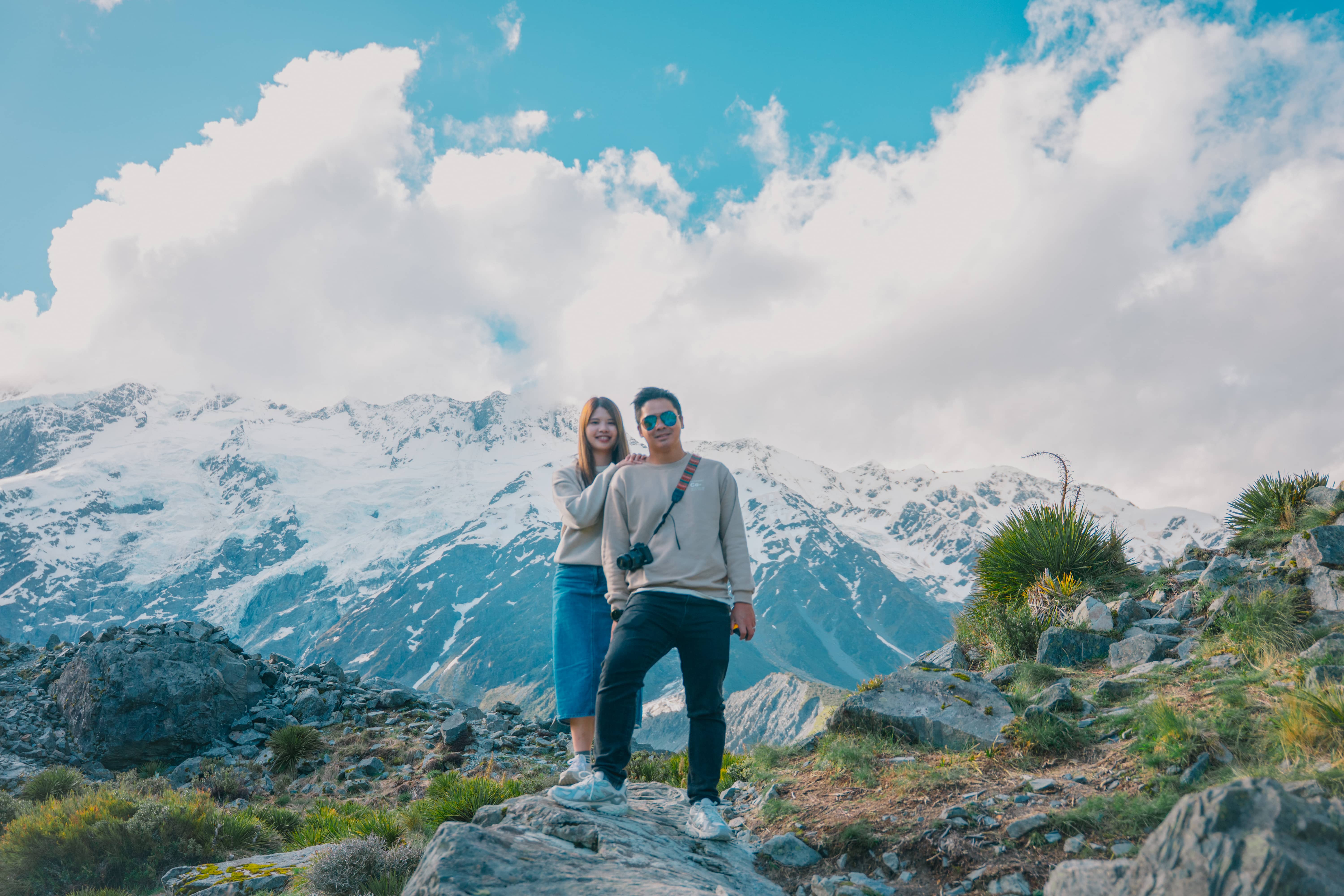 Couple standing on rocks in front of snow-capped Southern Alps peaks, New Zealand