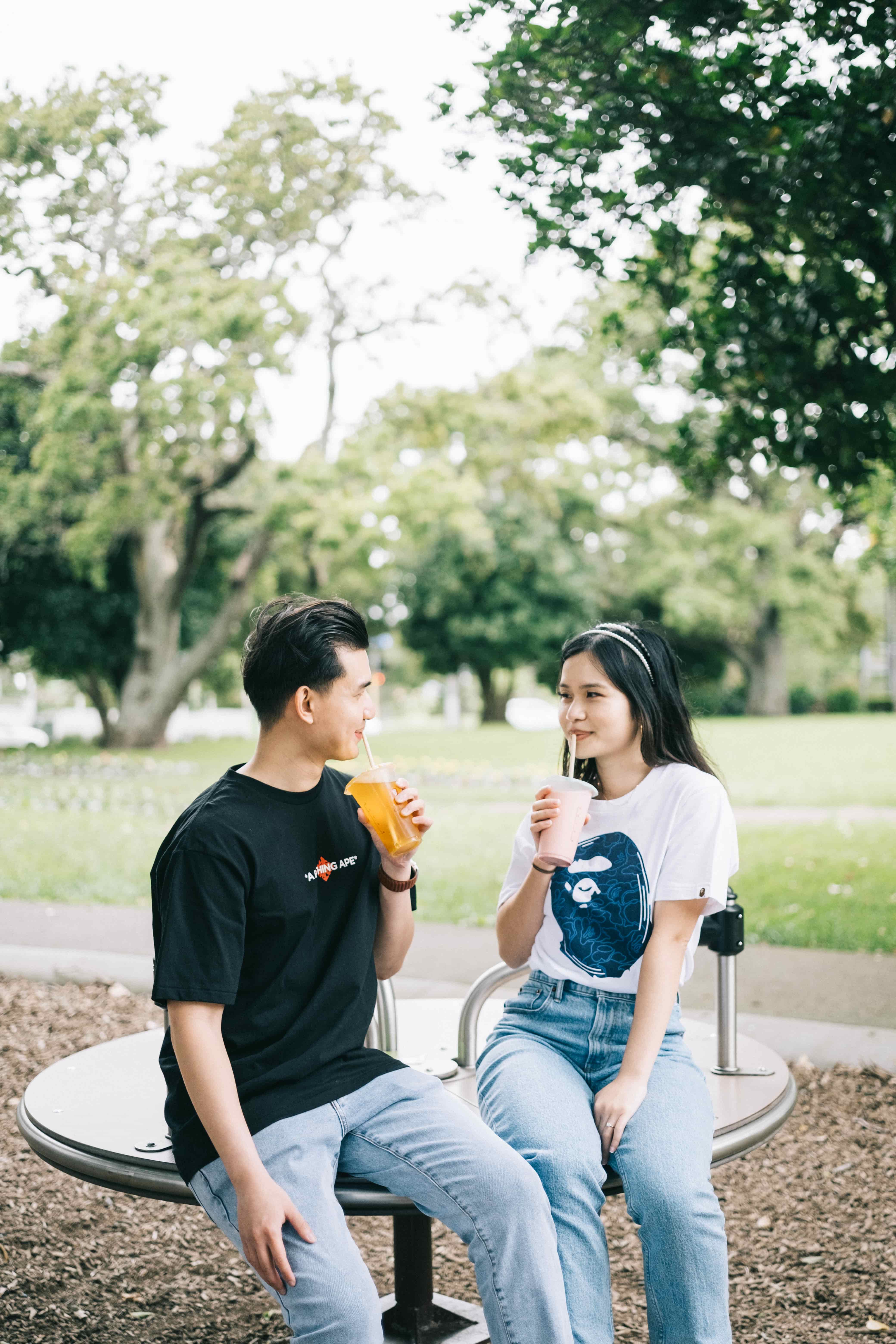 Suzen and Nick sipping drinks on a park roundabout with green lawns and trees behind
