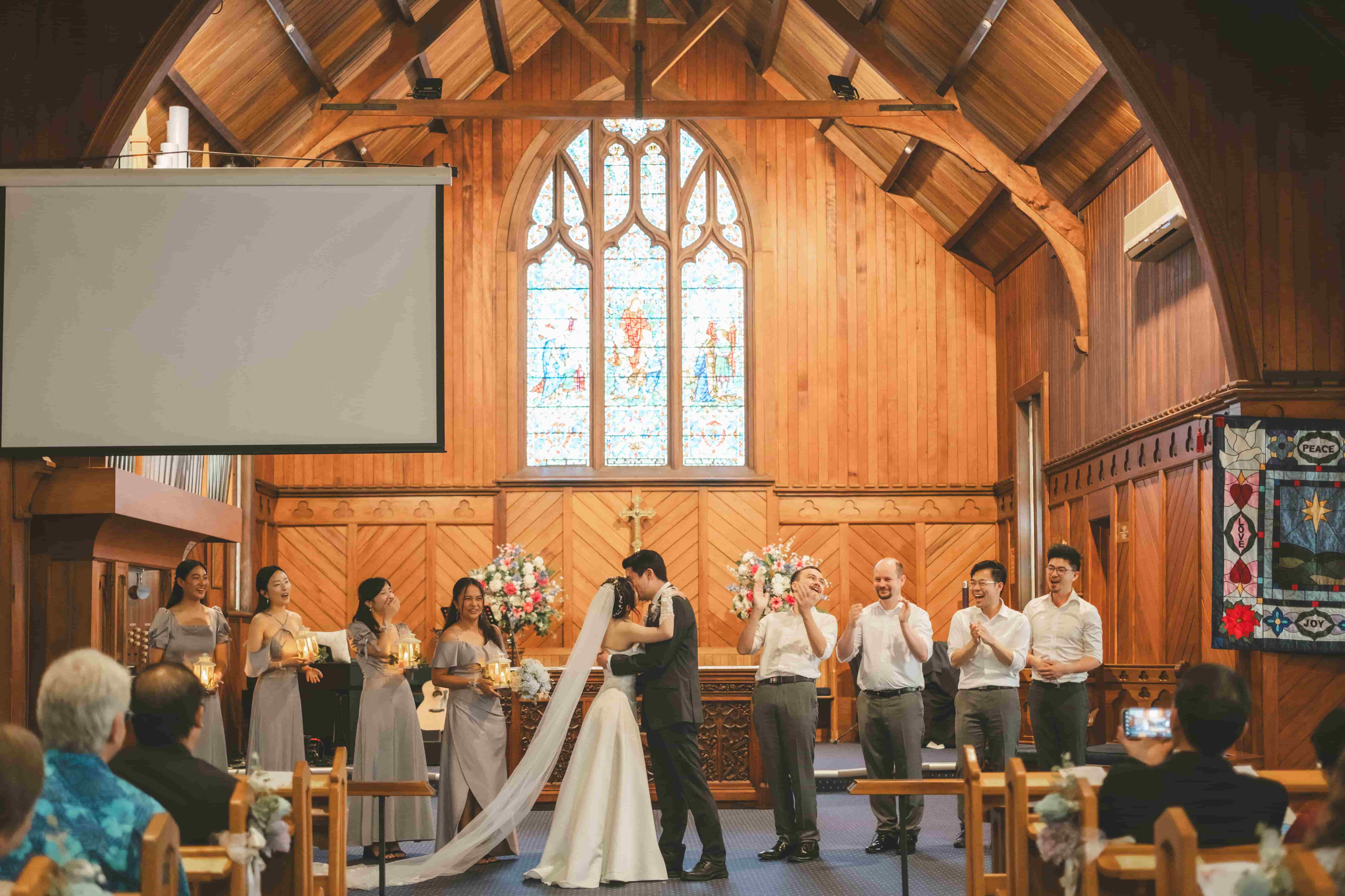 Hans and Chrystynn kissing at the front of the church as guests and the bridal party clap