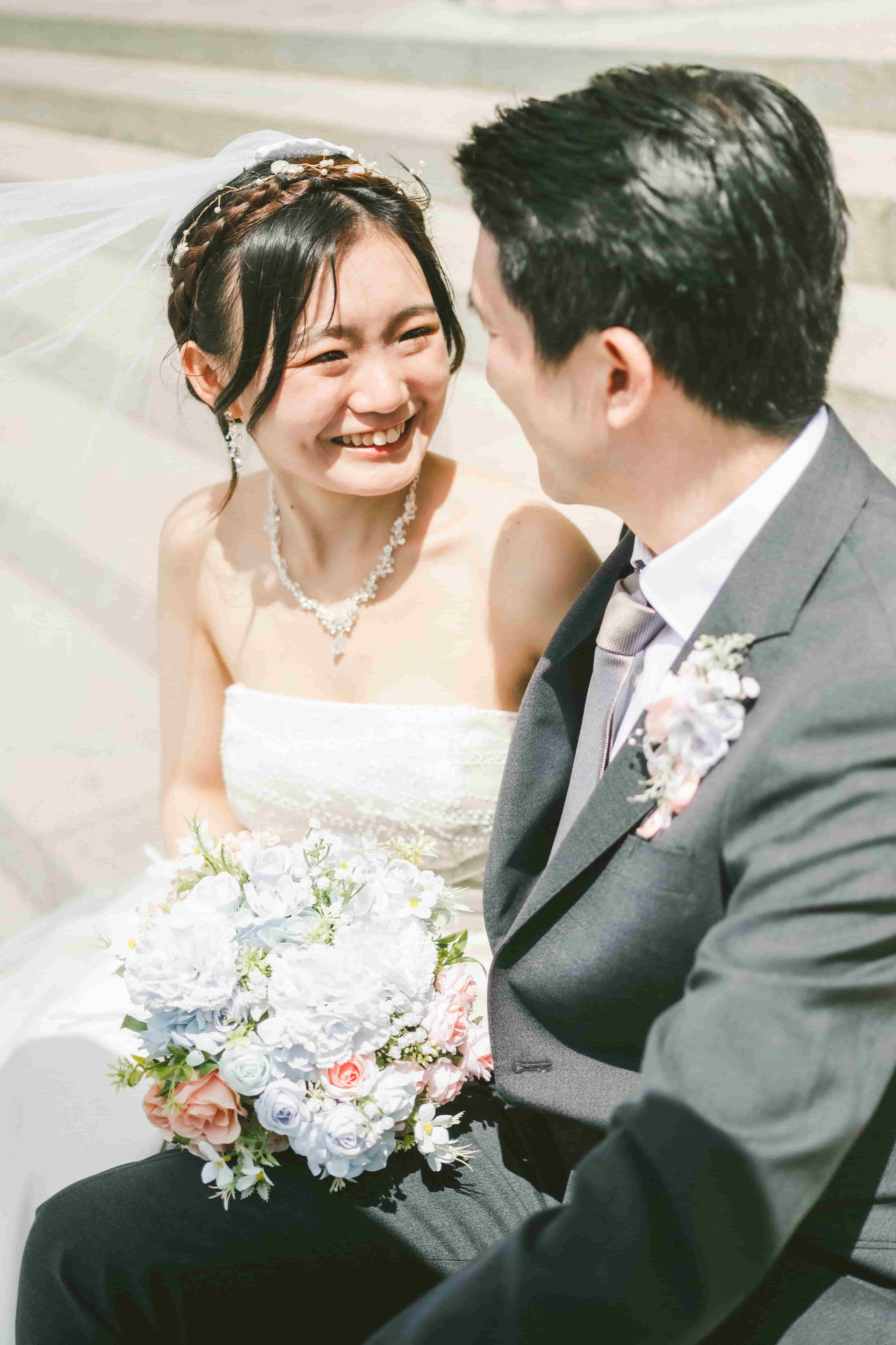 Chrystynn laughing up at Hans in bright sunshine, her veil lifting in the breeze