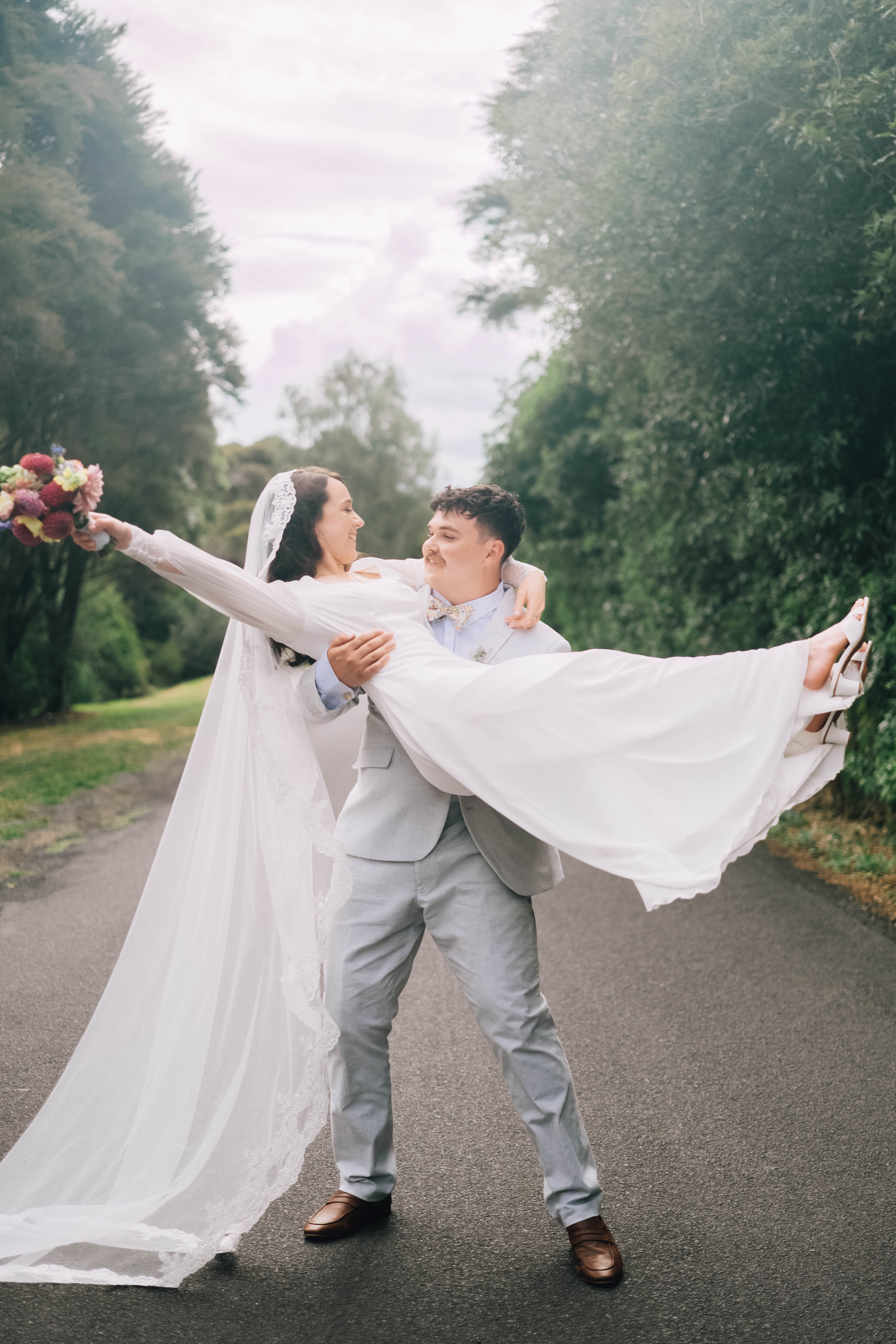 Joe lifting Mia off her feet on a country road, her bouquet held high and veil flowing