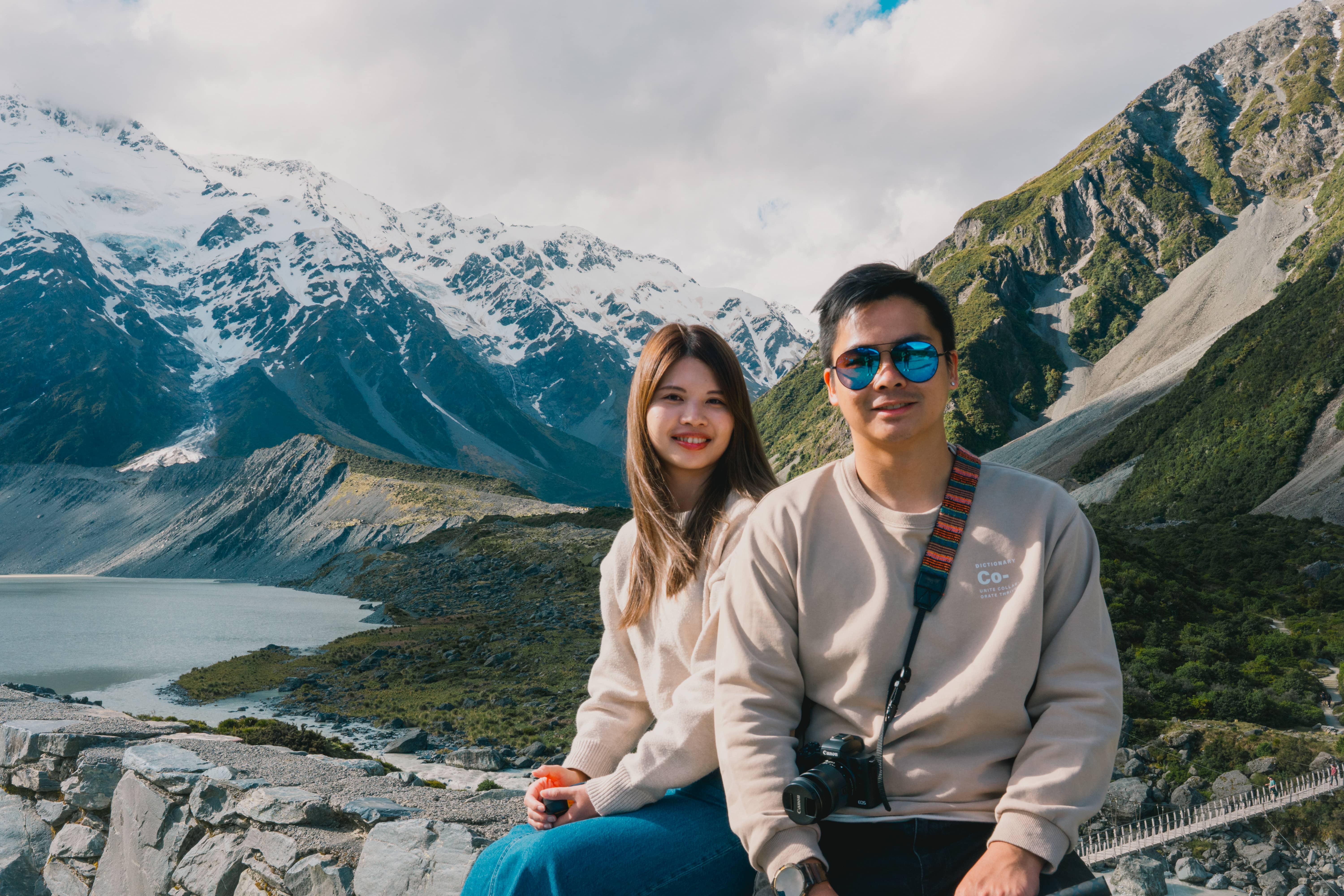 Julio and Kanis sitting on a rock wall above a glacial valley with snow-capped mountains