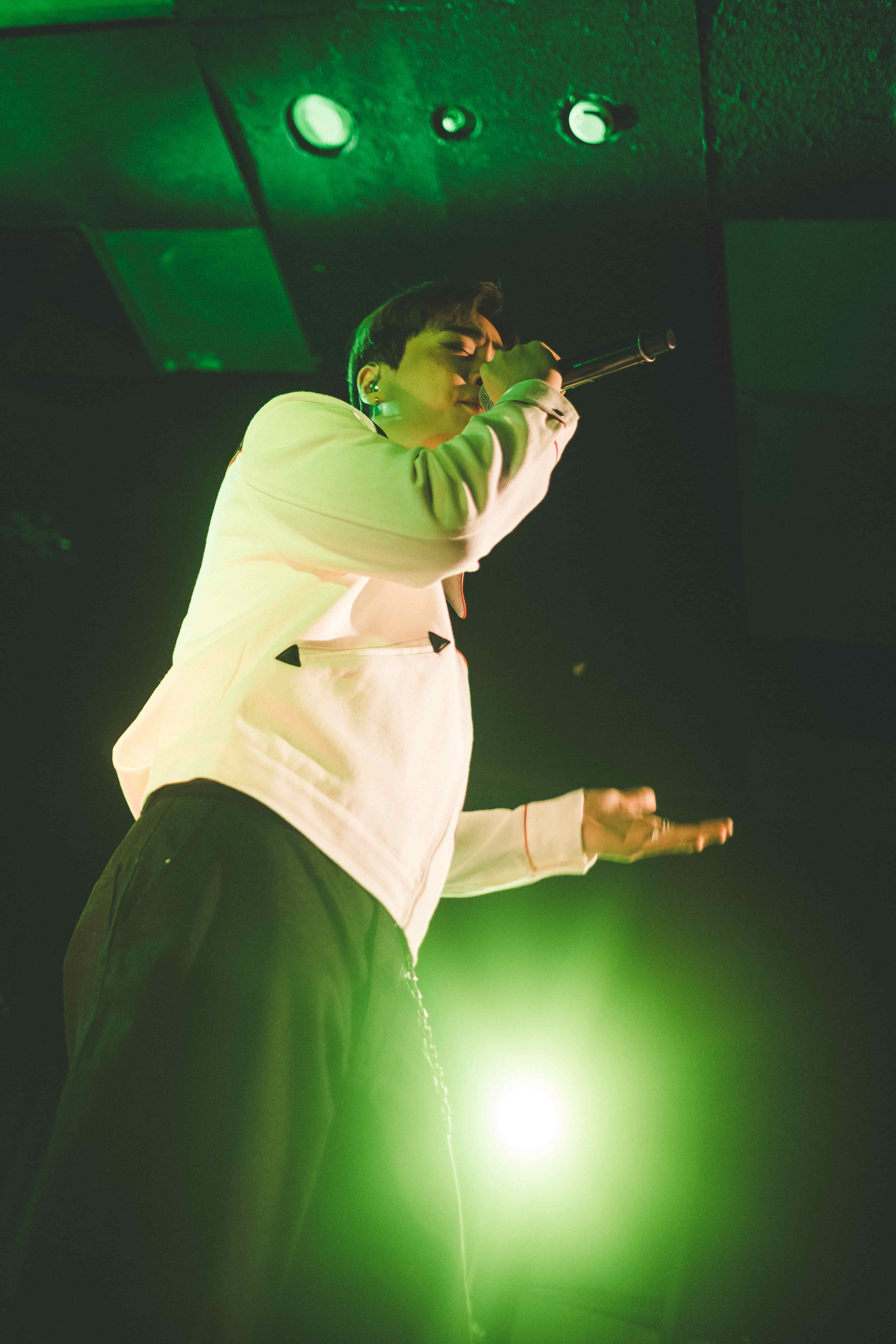 Junny leaning into his microphone, lit from below by a bright green stage light