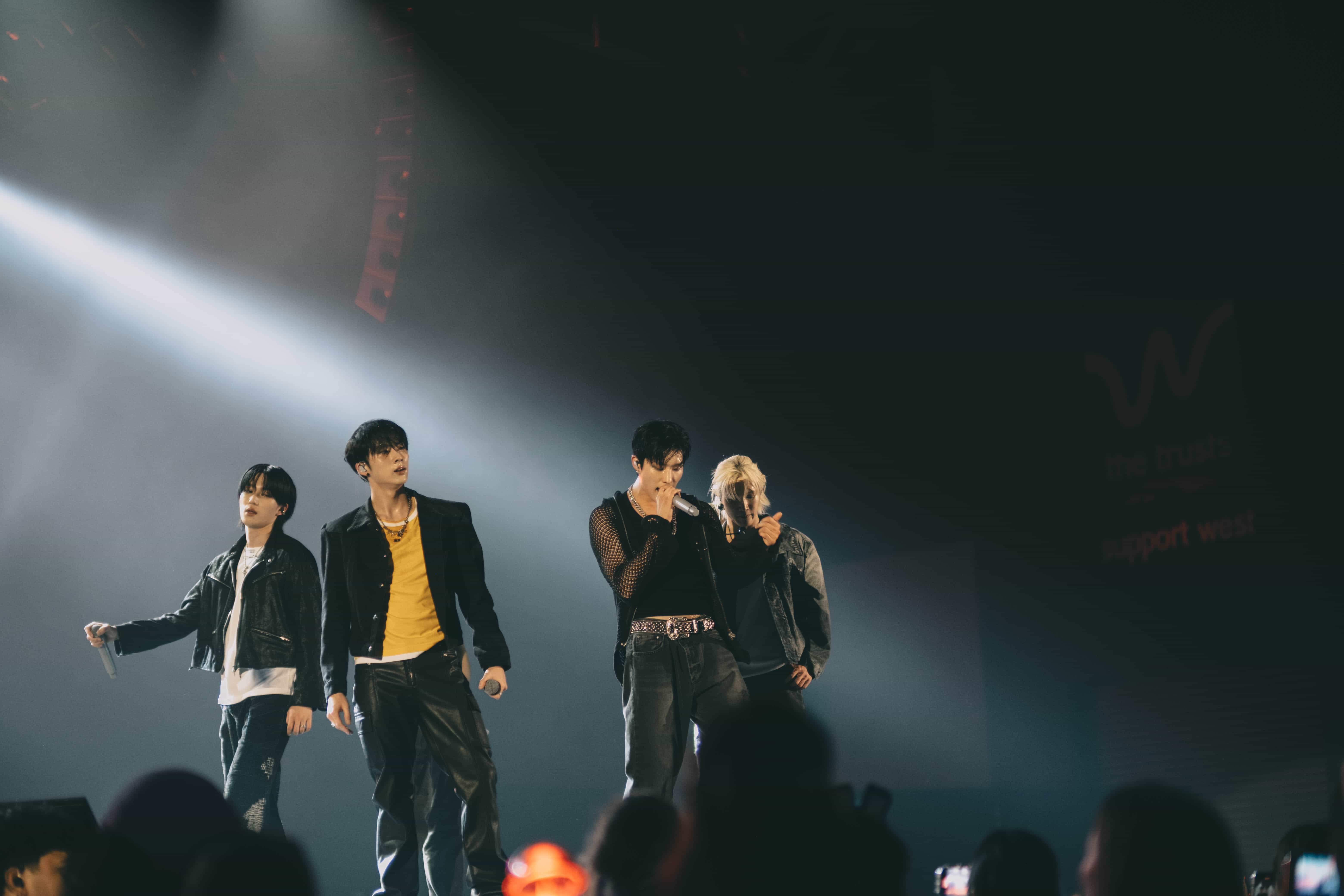 Four P1Harmony members in leather jackets dancing in a row under bright white haze