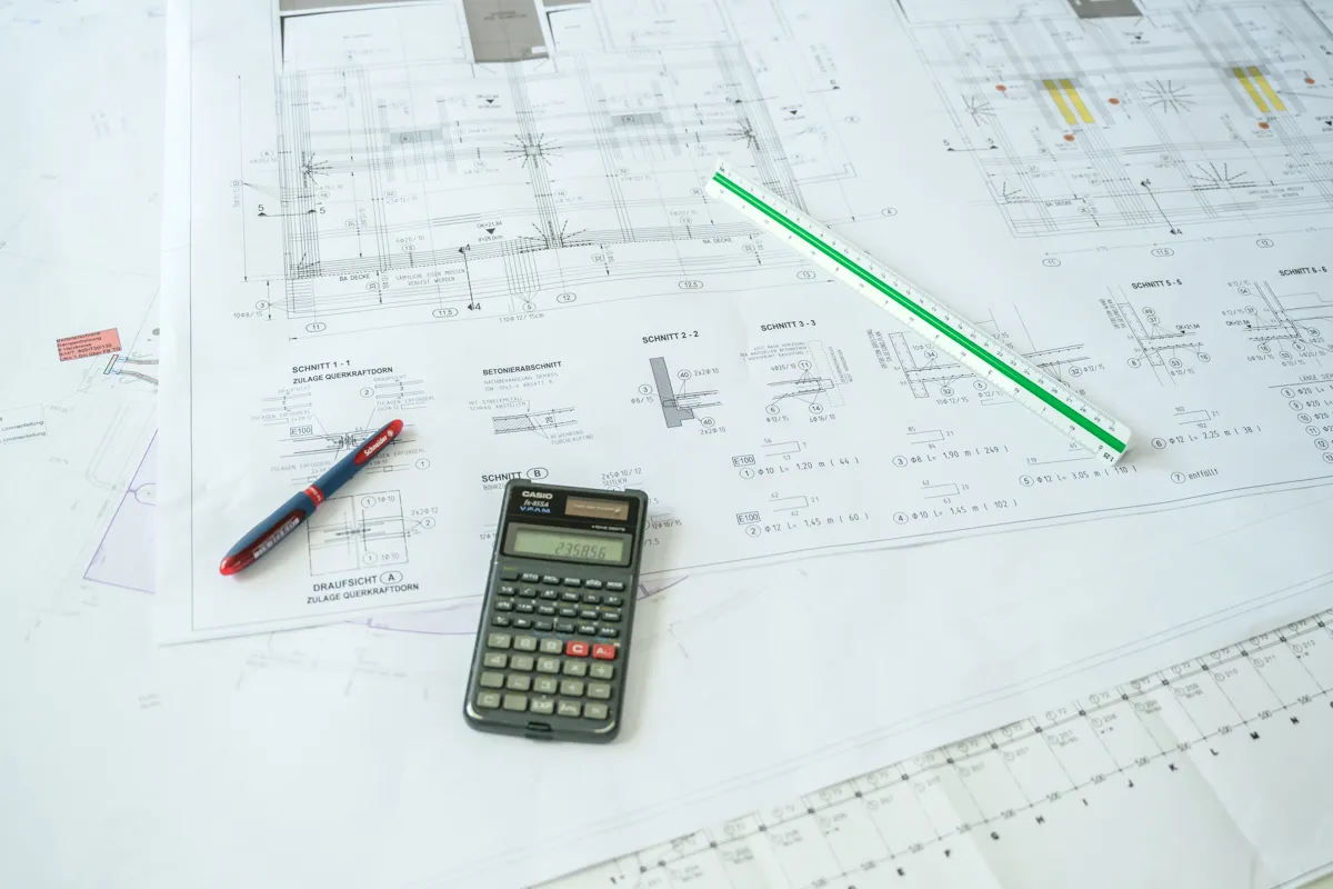 Taschenrechner, Stifte und Lineal auf einer Bauzeichnung liegend