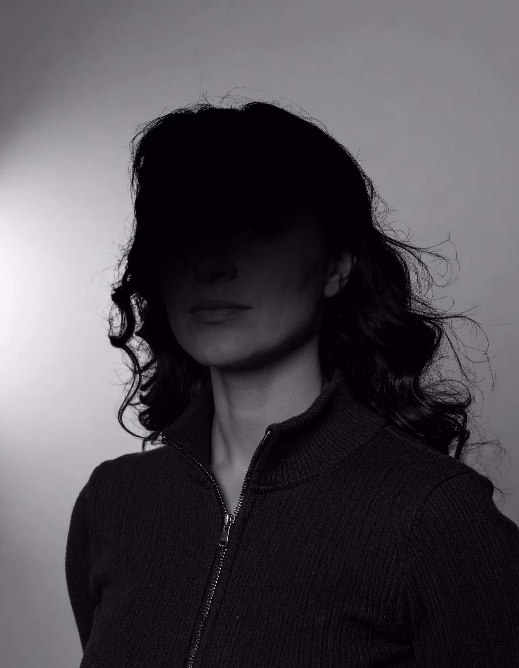 Portrait einer Person vor einem grauen Hintergrund mit einem starken Schatten im Gesicht