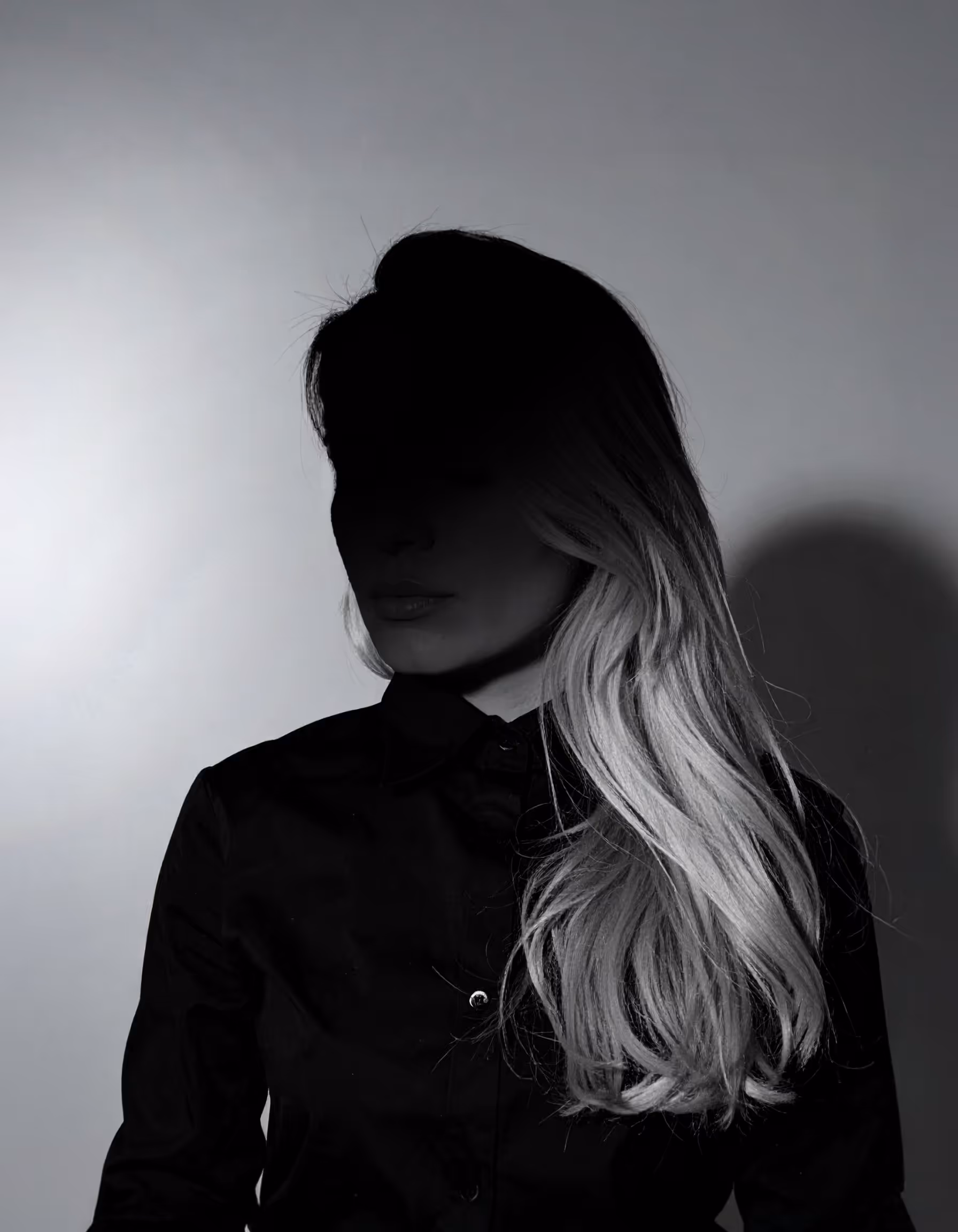 Portrait einer Person vor einem grauen Hintergrund mit einem starken Schatten im Gesicht