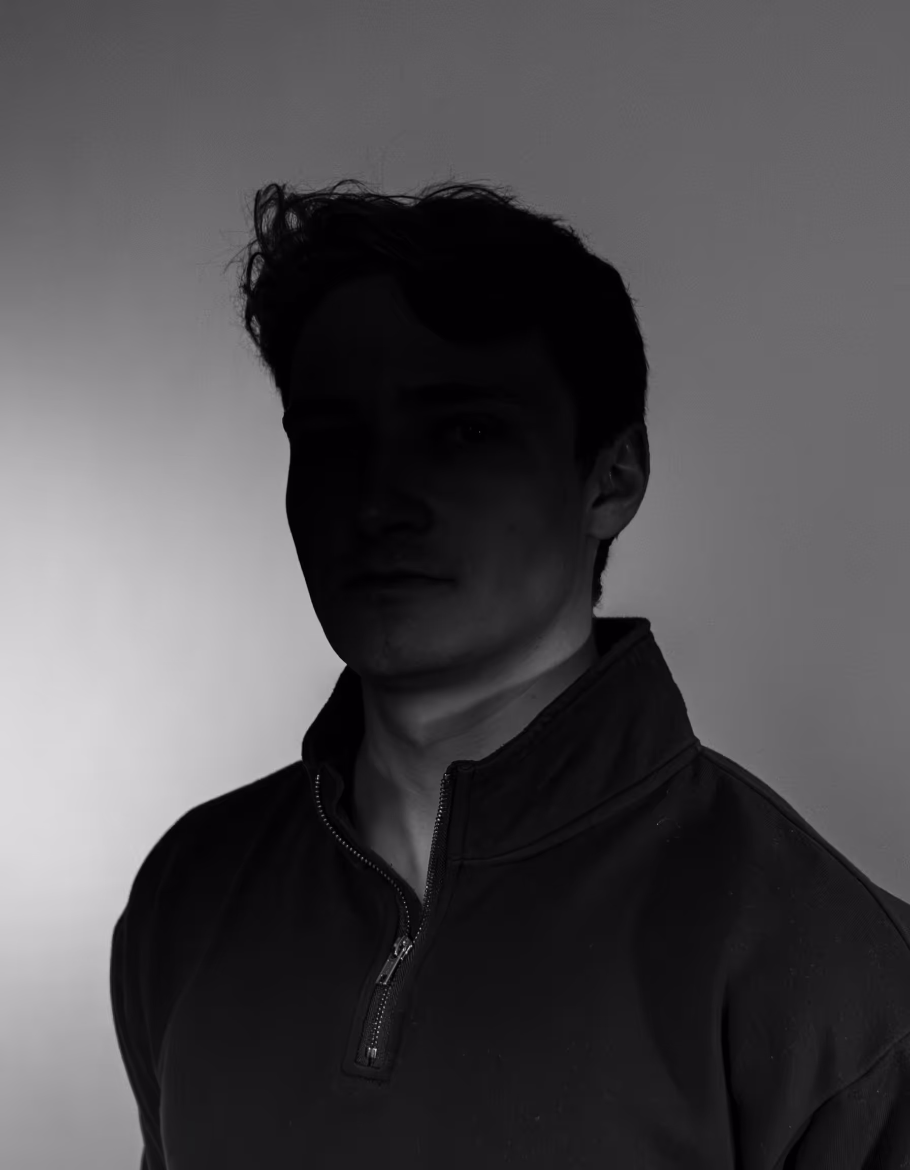 Portrait einer Person vor einem grauen Hintergrund mit einem starken Schatten im Gesicht