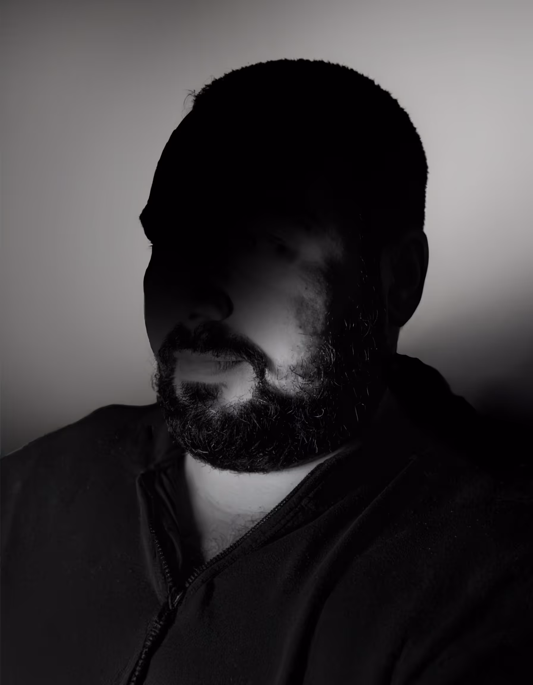 Portrait einer Person vor einem grauen Hintergrund mit einem starken Schatten im Gesicht