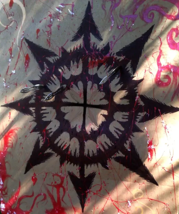 Black abstract star-like symbol with jagged edges and a cross in the center, painted on a surface with red and purple paint splatters.
