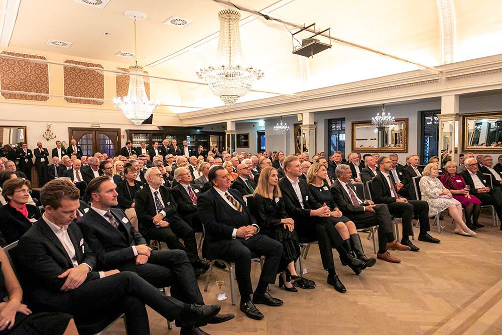 Festlich gekleidete Gäste sitzen in einem prunkvollen Saal mit Kronleuchtern und lauschen einer Veranstaltung, VLK Herrenessen 2024.