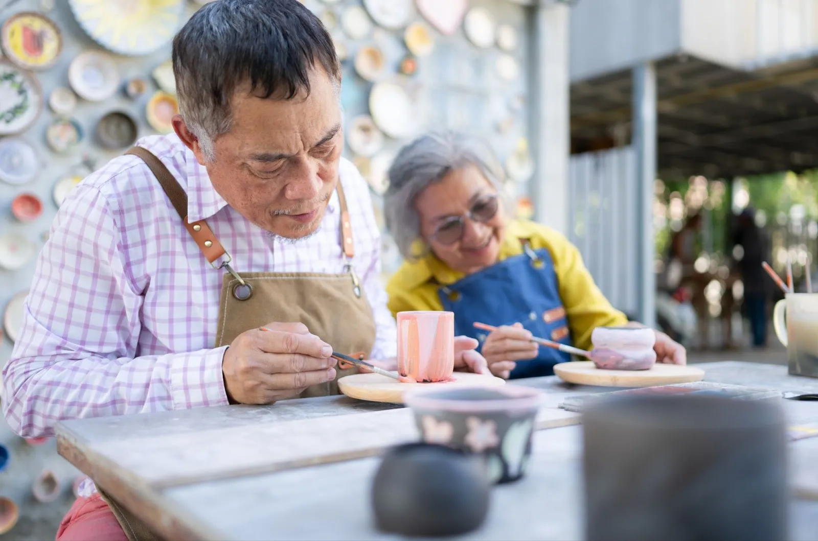 An elderly couple enjoys pottery painting together, promoting senior mental health awareness through creative activities for aging loved ones, supported by tools like the Caily app.