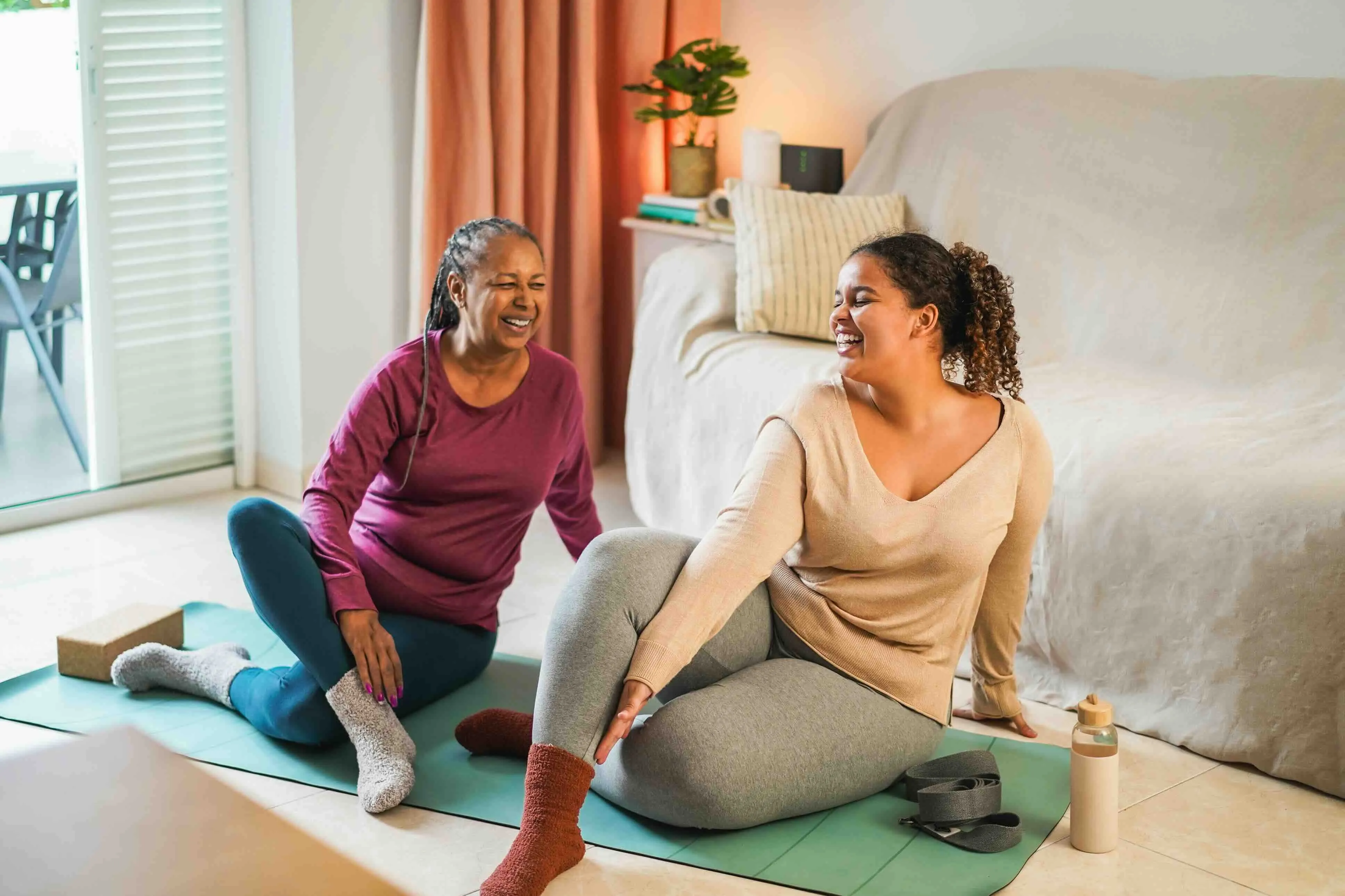 Smiling mother and daughter doing yoga together at home—an uplifting example of how family caregivers can reduce stress and prevent caregiver fatigue through self-care and connection