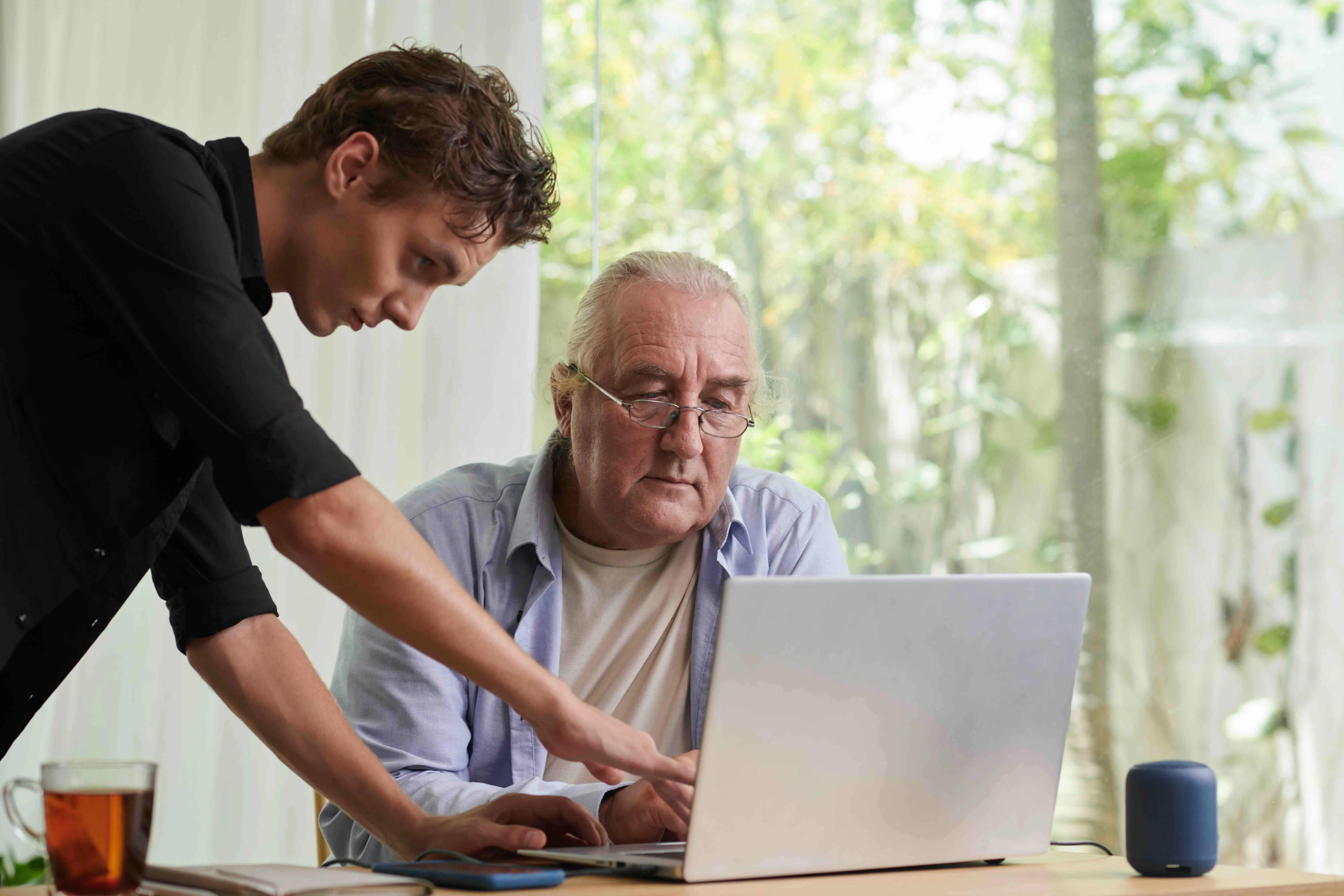 Young man assisting senior father with end-of-life planning on a laptop, discussing end-of-life legal documents and how to create a will online.