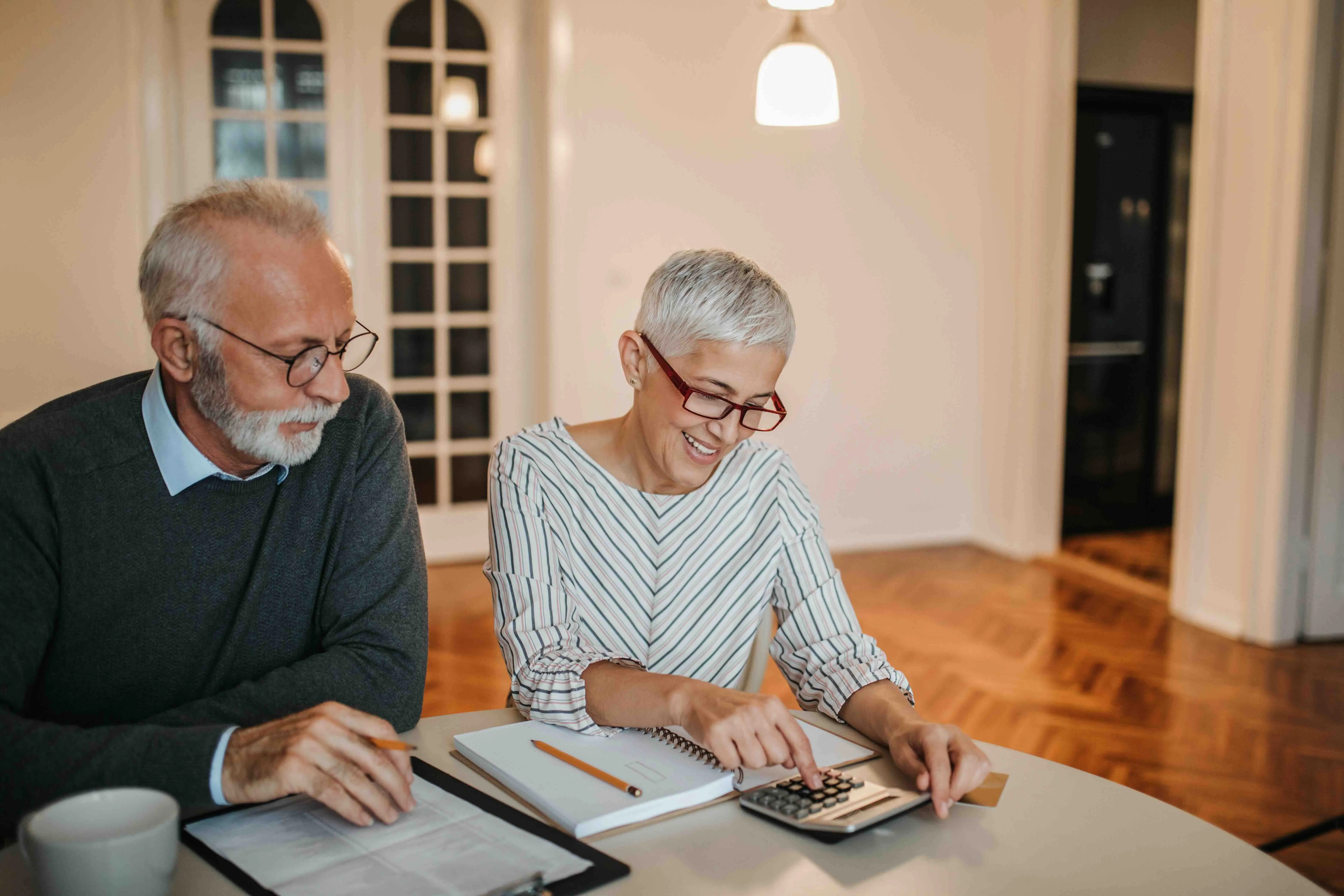 Older couple reviewing expenses and using a calculator at home, illustrating financial help for caregivers and budgeting for elderly care.