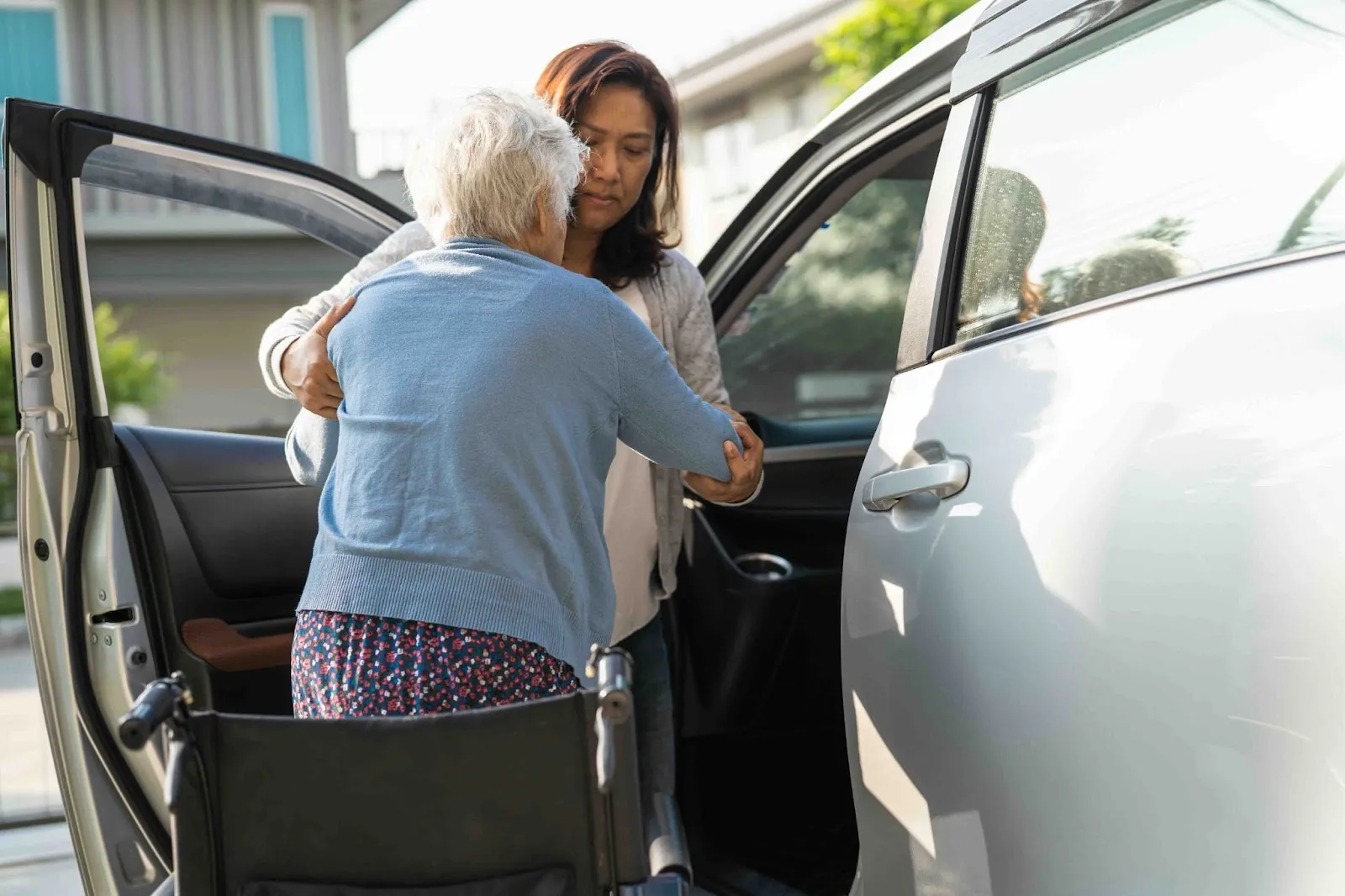 Family caregiver assisting elderly woman into a car, highlighting hidden caregiving costs like travel and the need for financial help for caregivers.
