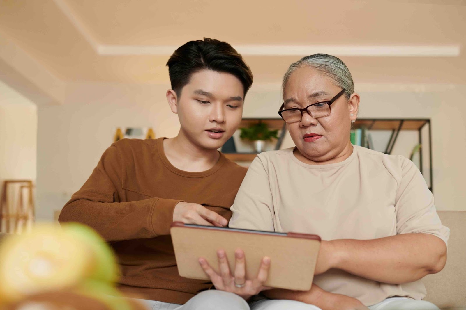 Adult son helping his elderly mother navigate end-of-life planning on a digital tablet, illustrating family communication, advance care directives, and documenting last wishes together.