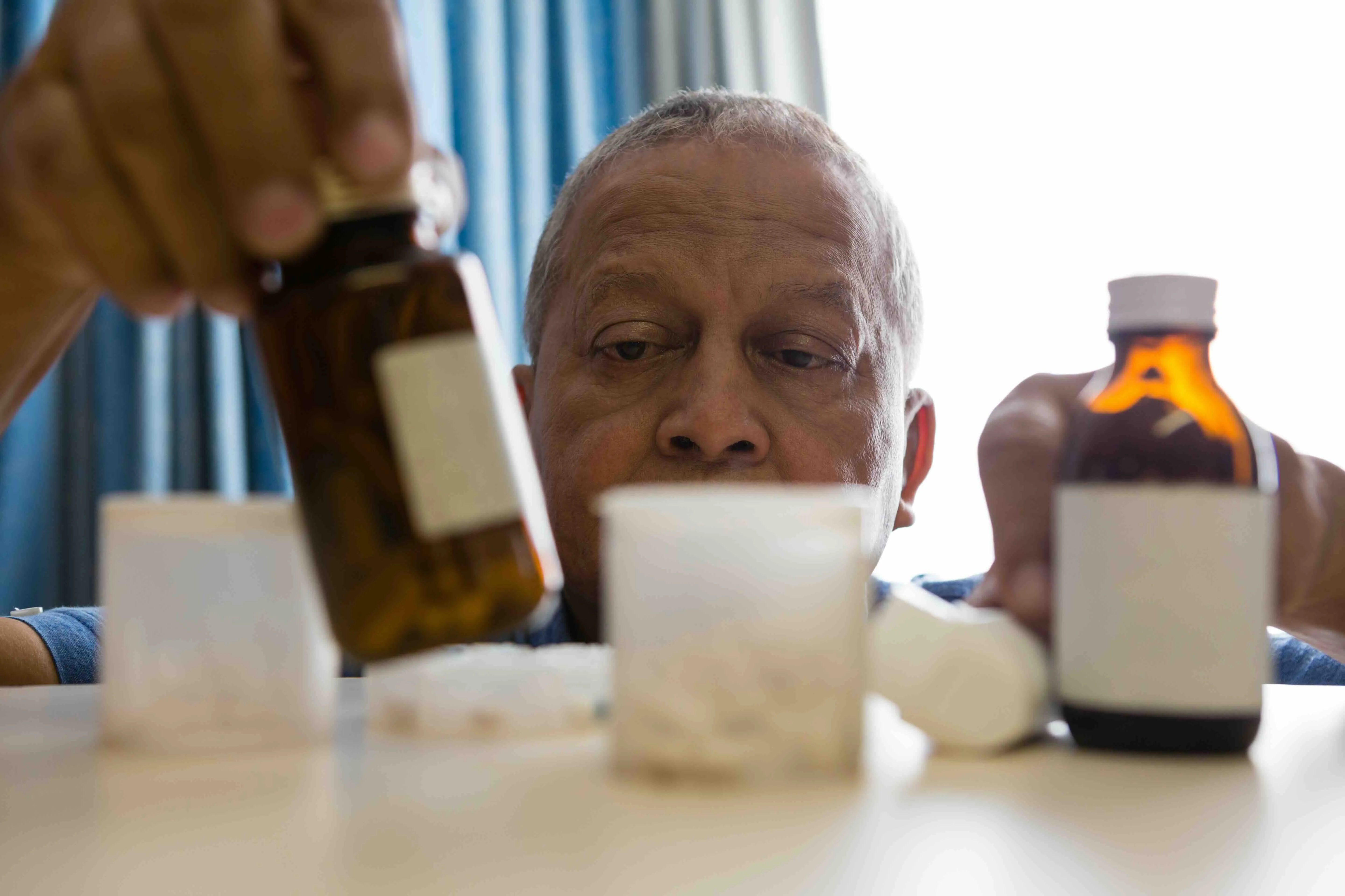 Senior man organizing his daily medication with multiple pill bottles on a table, illustrating the importance of a medication calendar and effective medication management for elderly care.