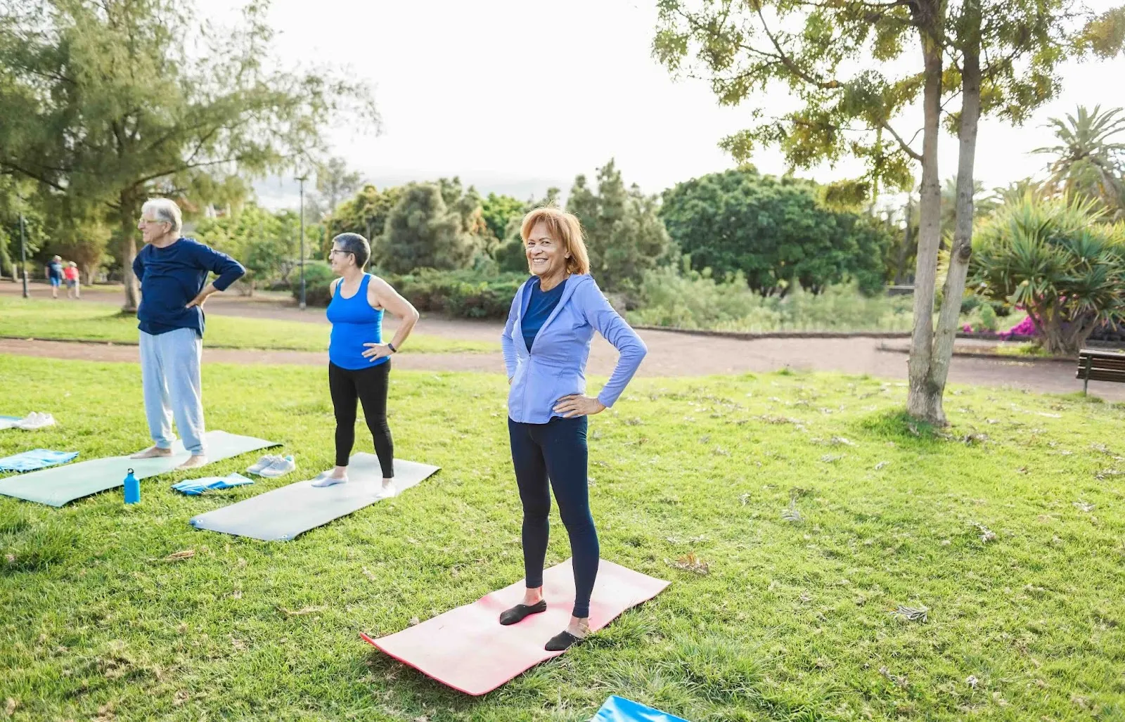 Group of seniors participating in outdoor balance and mobility exercises on yoga mats in a park, promoting fall prevention and physical activity for older adults with limited mobility.