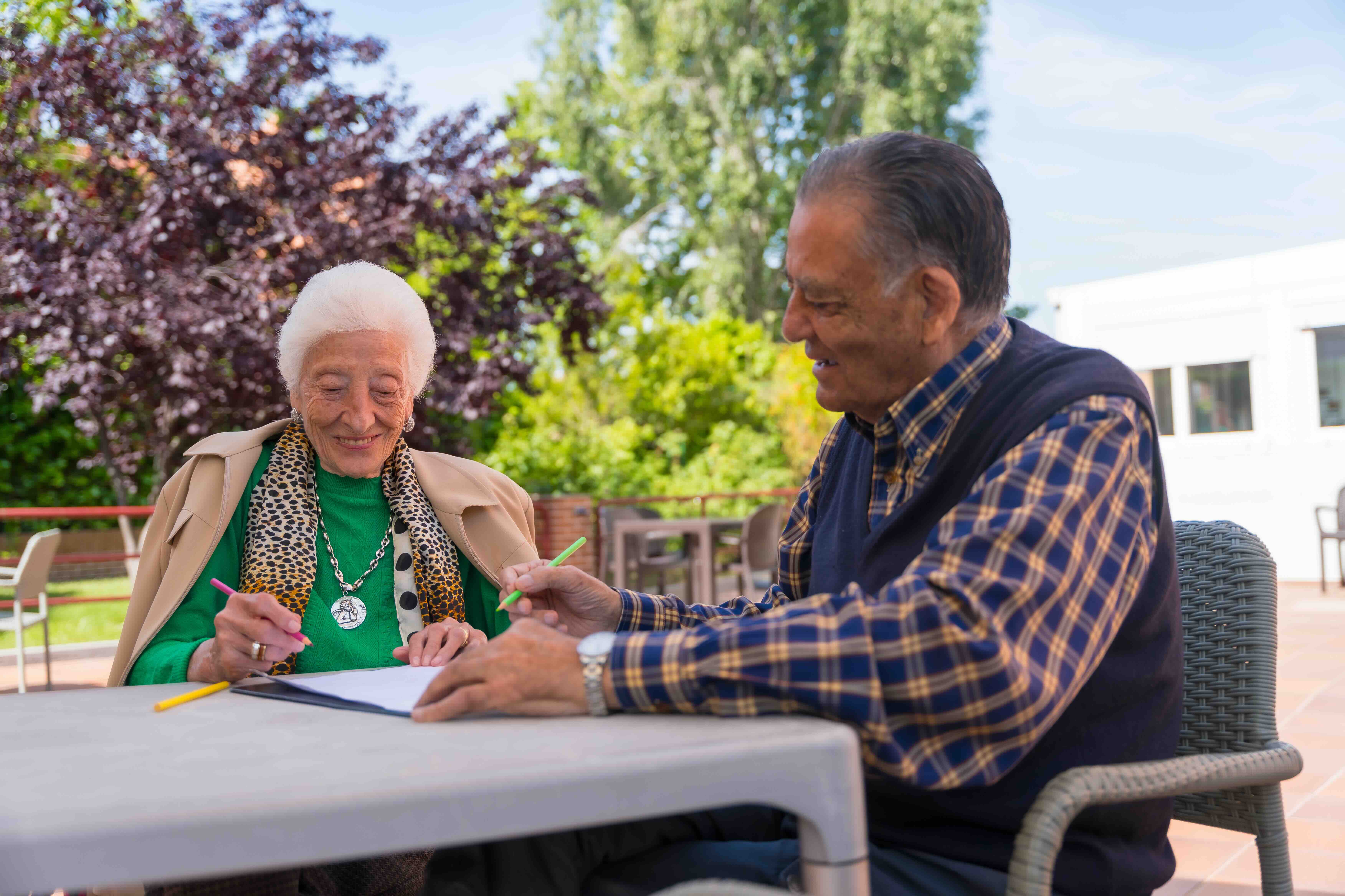 Two elderly people enjoying dementia care at home while drawing together outdoors, demonstrating creative activities for different dementia stages in a calm, supportive environment.