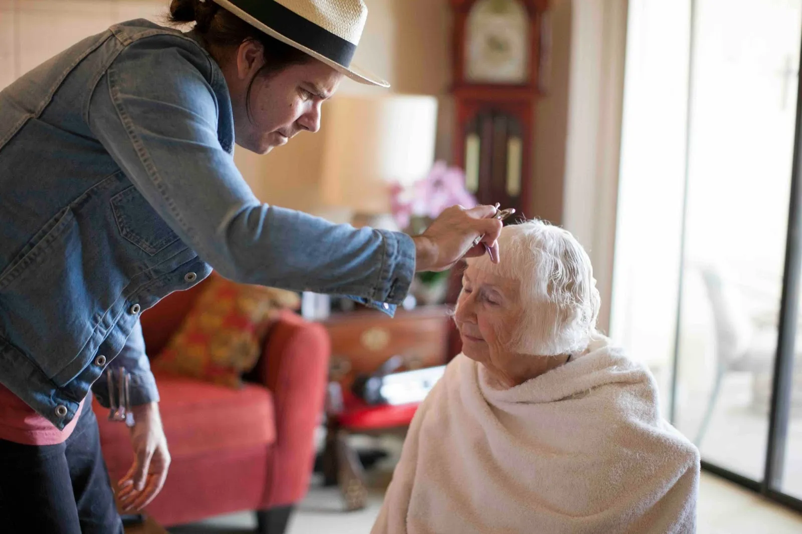 Caregiver providing in-home dementia care by gently cutting an elderly woman’s hair, demonstrating supportive routines for later stages of dementia care at home.