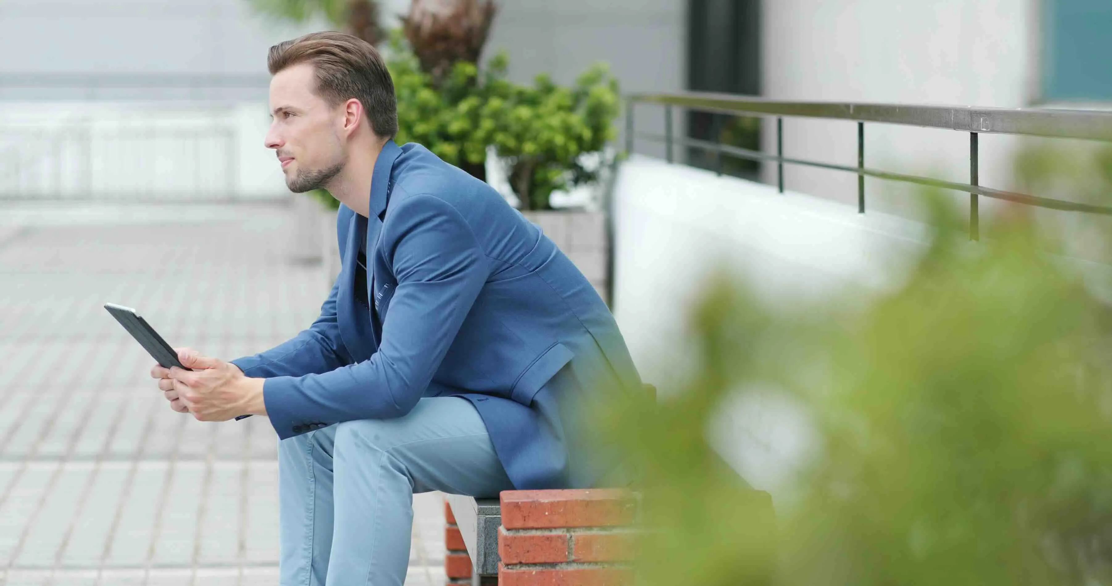 Man in blue suit sitting outside holding a tablet, appearing thoughtful—illustrating emotional fatigue or detachment related to burnout vs depression, high functioning depression, or signs of burnout.