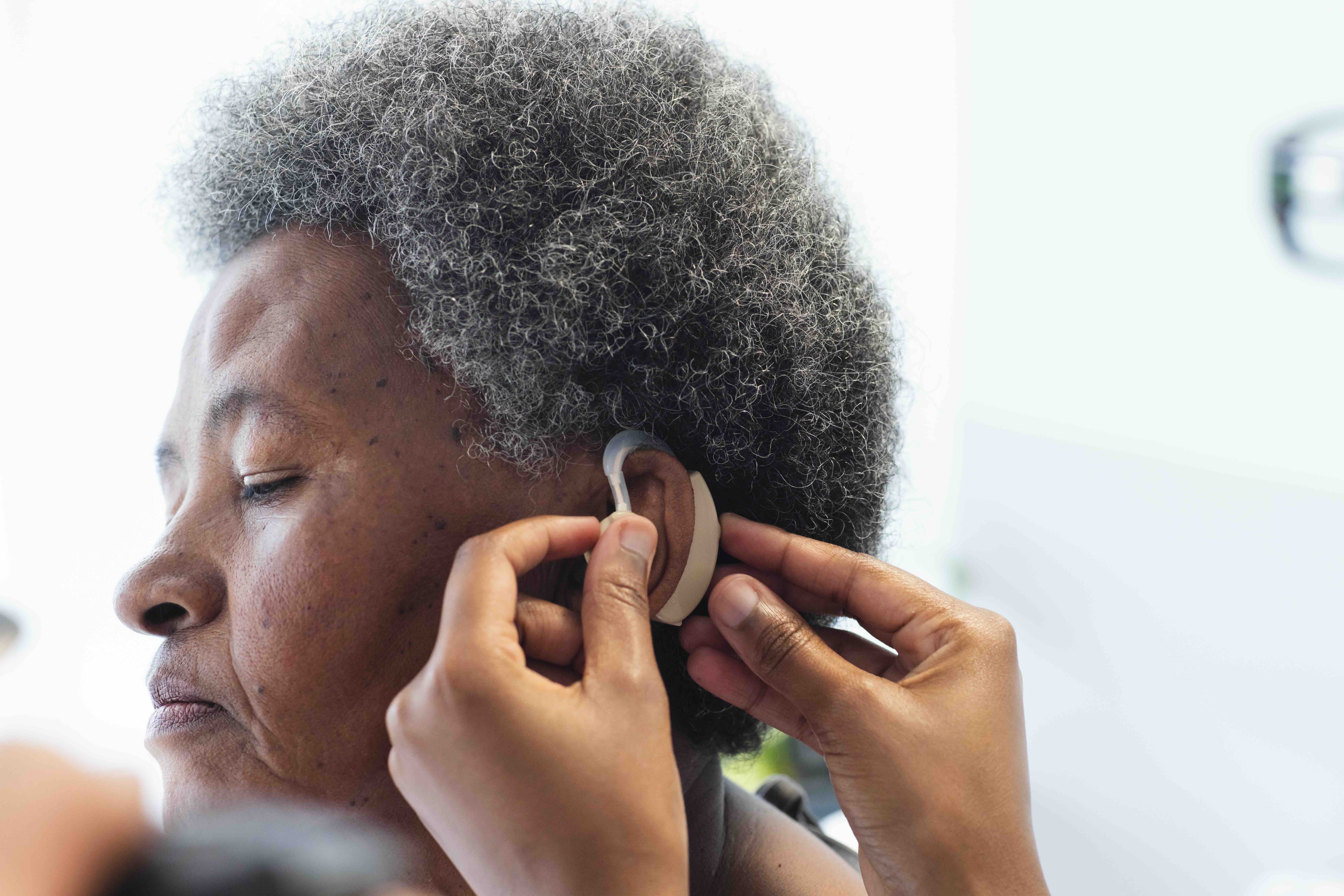 Audiologist fitting the best hearing aids behind the ear of an older woman, showing how hearing aids for tinnitus and advanced models improve hearing.
