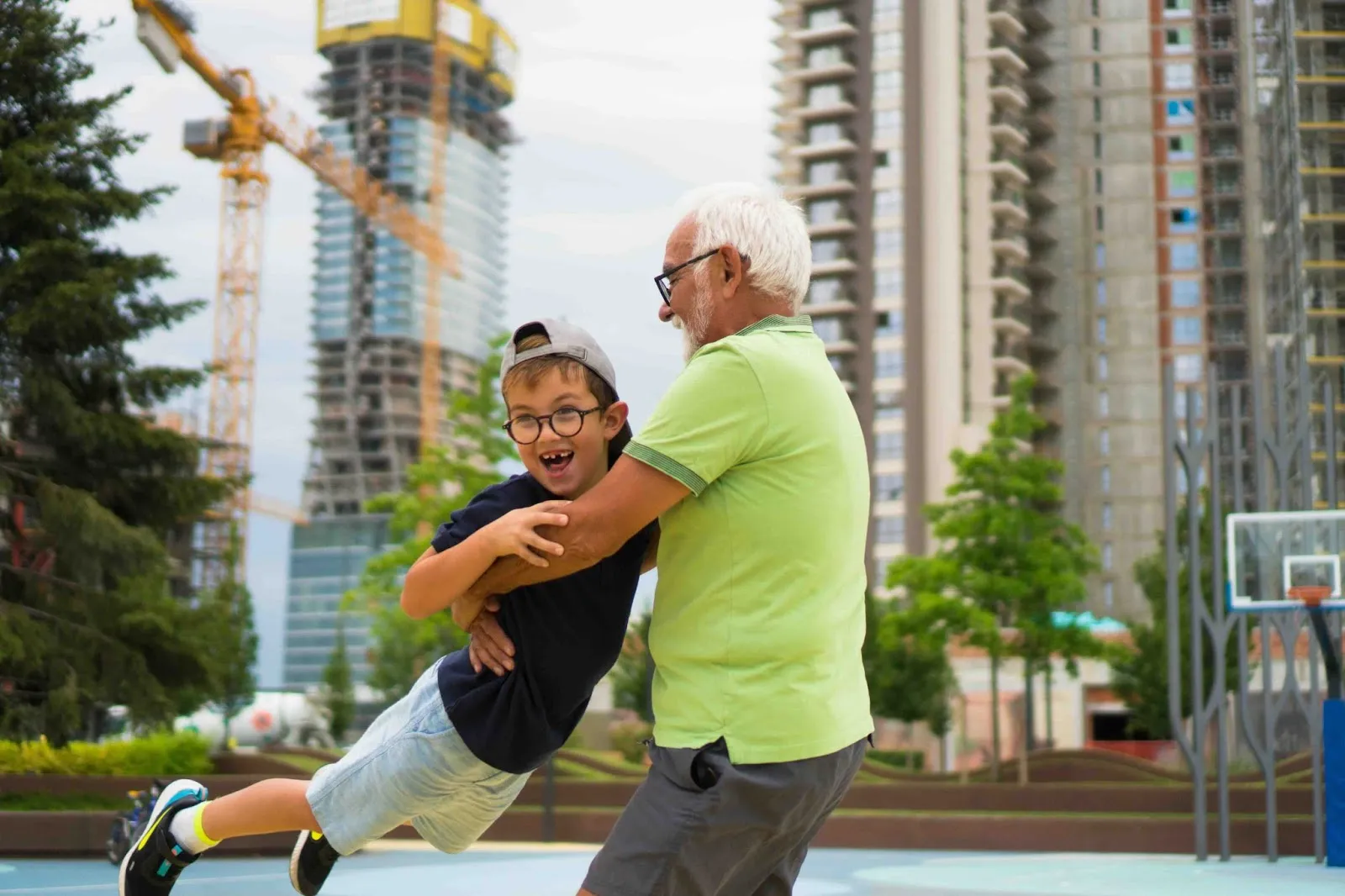 Grandfather joyfully swinging his grandson at a playground, symbolizing the sandwich generation and the bond between aging parents and younger children cared for by midlife caregivers.