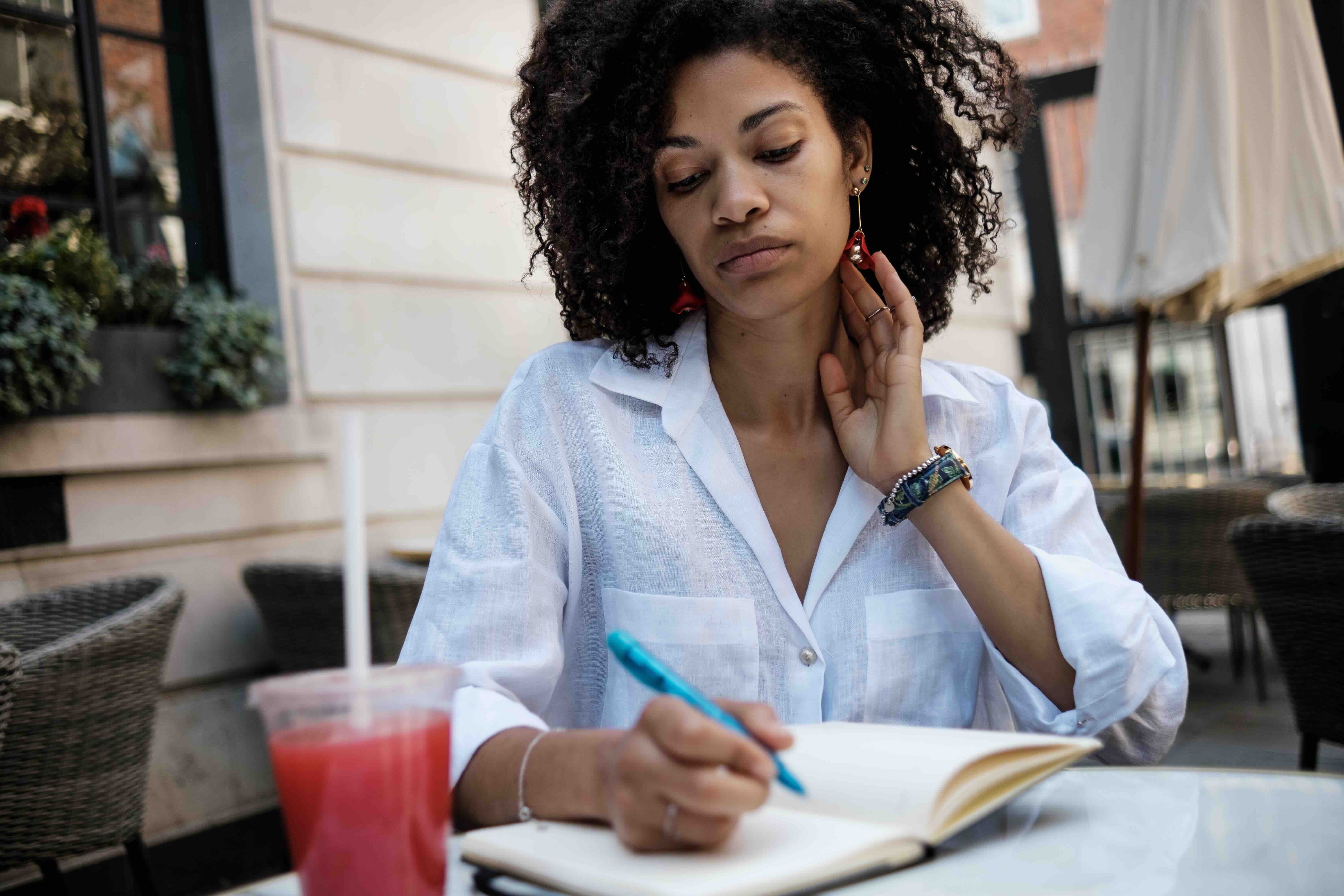 Woman writing an obituary draft in a notebook at an outdoor café, showing the process of writing an obituary and reflecting on how to write an obituary with care.