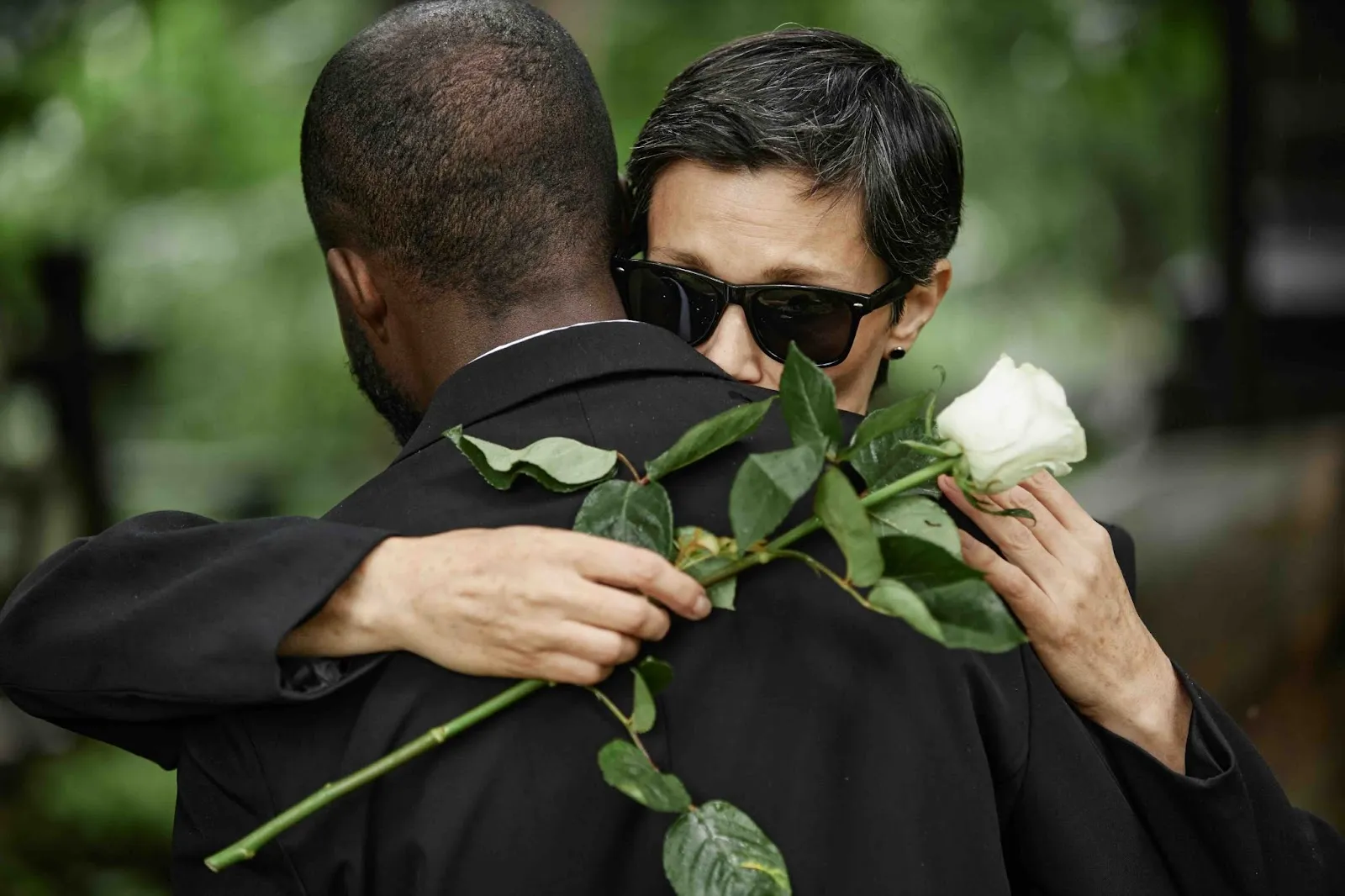 Grieving woman holding a white rose embraces a man at a funeral, symbolizing loss and remembrance often shared through obituaries and guidance on how to announce a death.