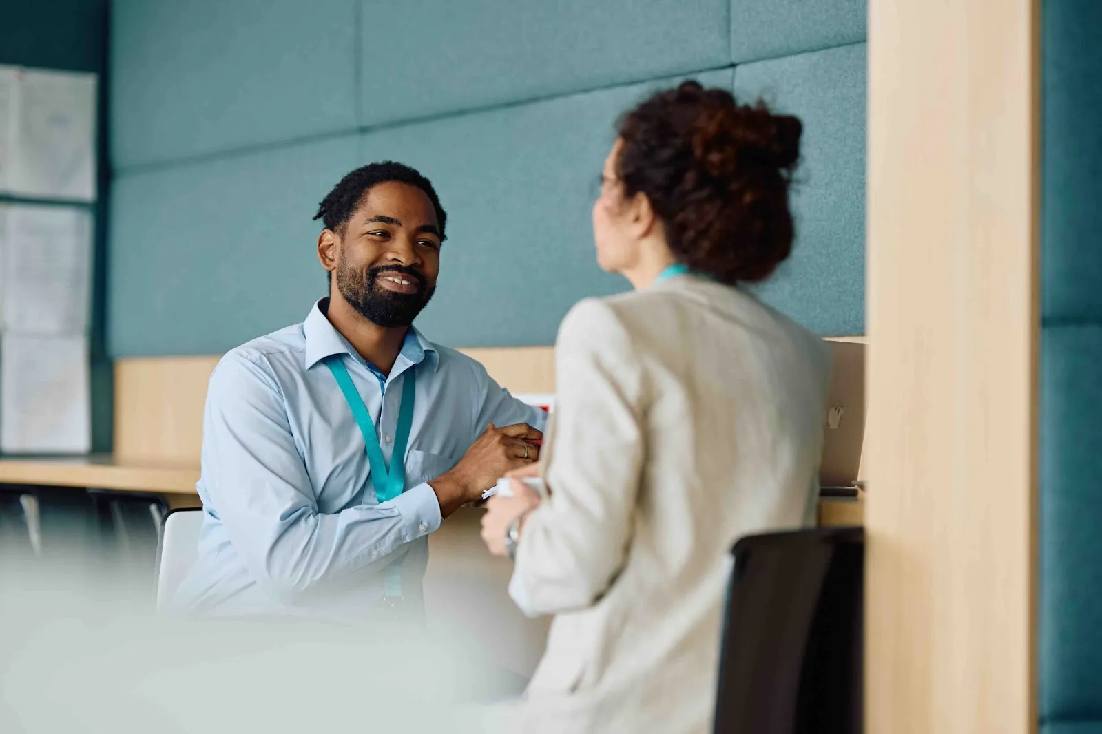 A smiling male professional in conversation with a female colleague in a modern office setting, representing supportive workplace dialogue about caregiving needs.)