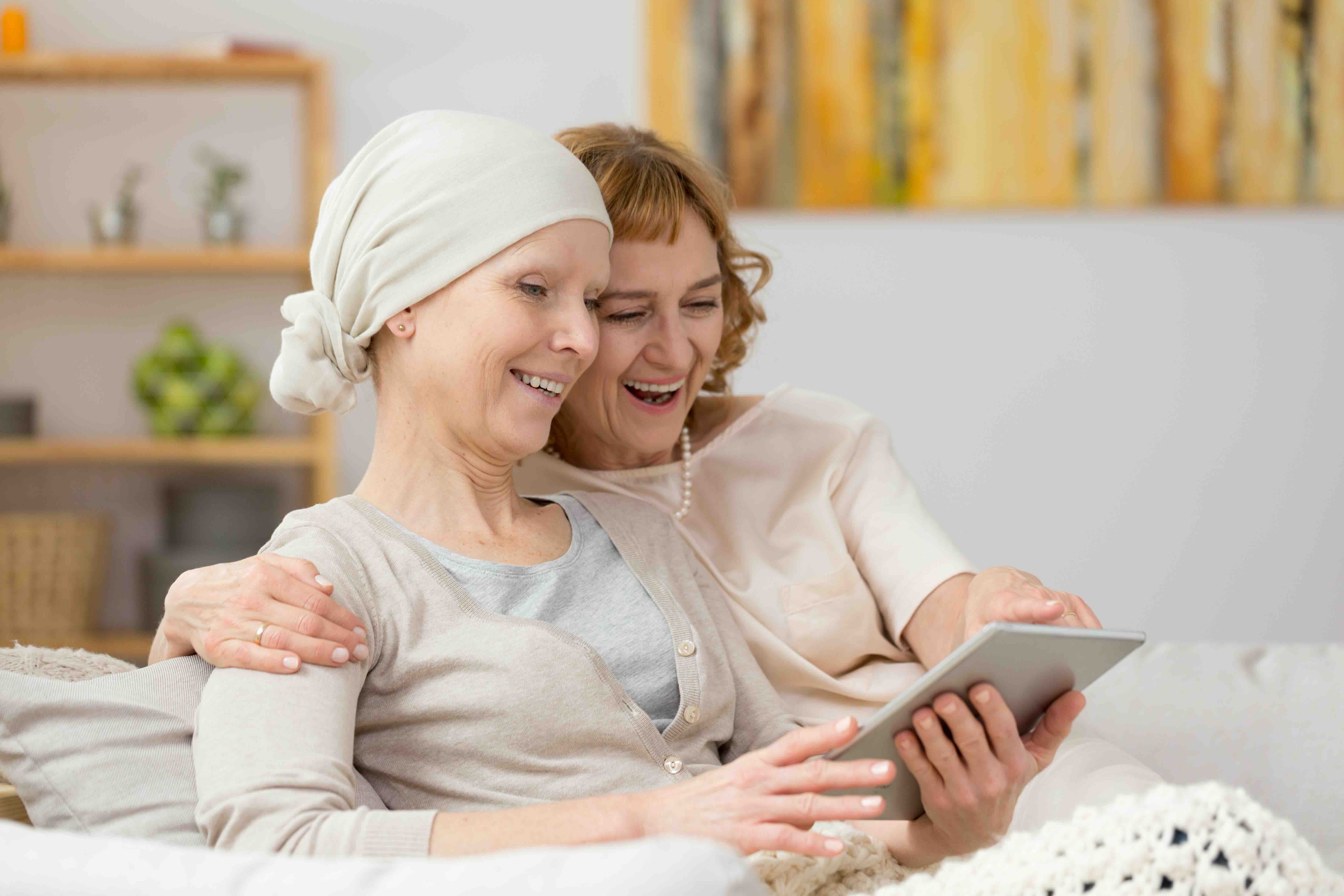 Caregiver for breast cancer patient offering emotional support at home — two women smiling while using a tablet together, showing compassion and connection during chemo care.