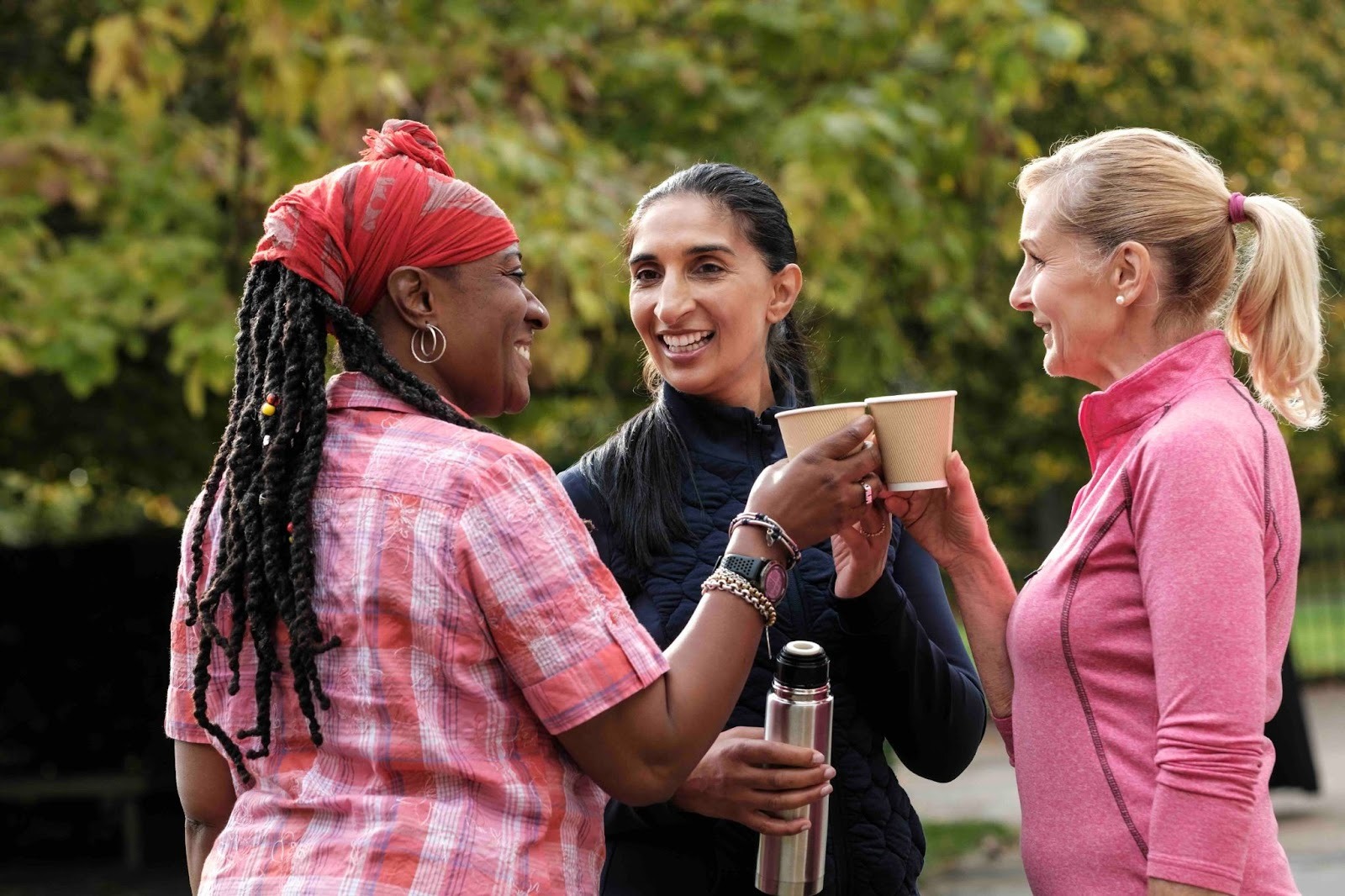 hree women smiling and clinking coffee cups outdoors, representing connection, friendship, and caregiver support during National Family Caregiver Awareness Month 2025