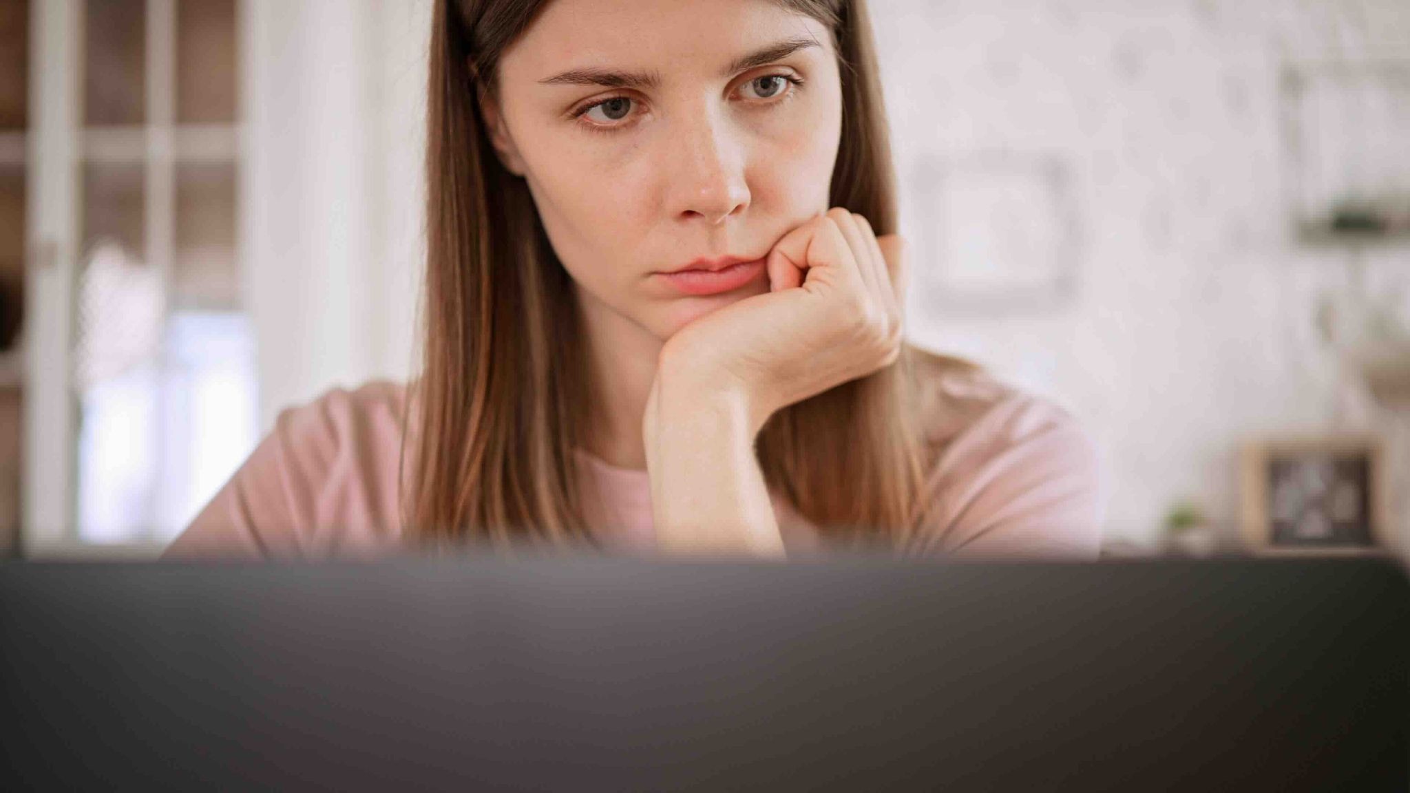 A young woman looks tired and thoughtful while staring at her laptop, reflecting the emotional strain many experience before finding help through caregiver support groups and support groups for caregivers