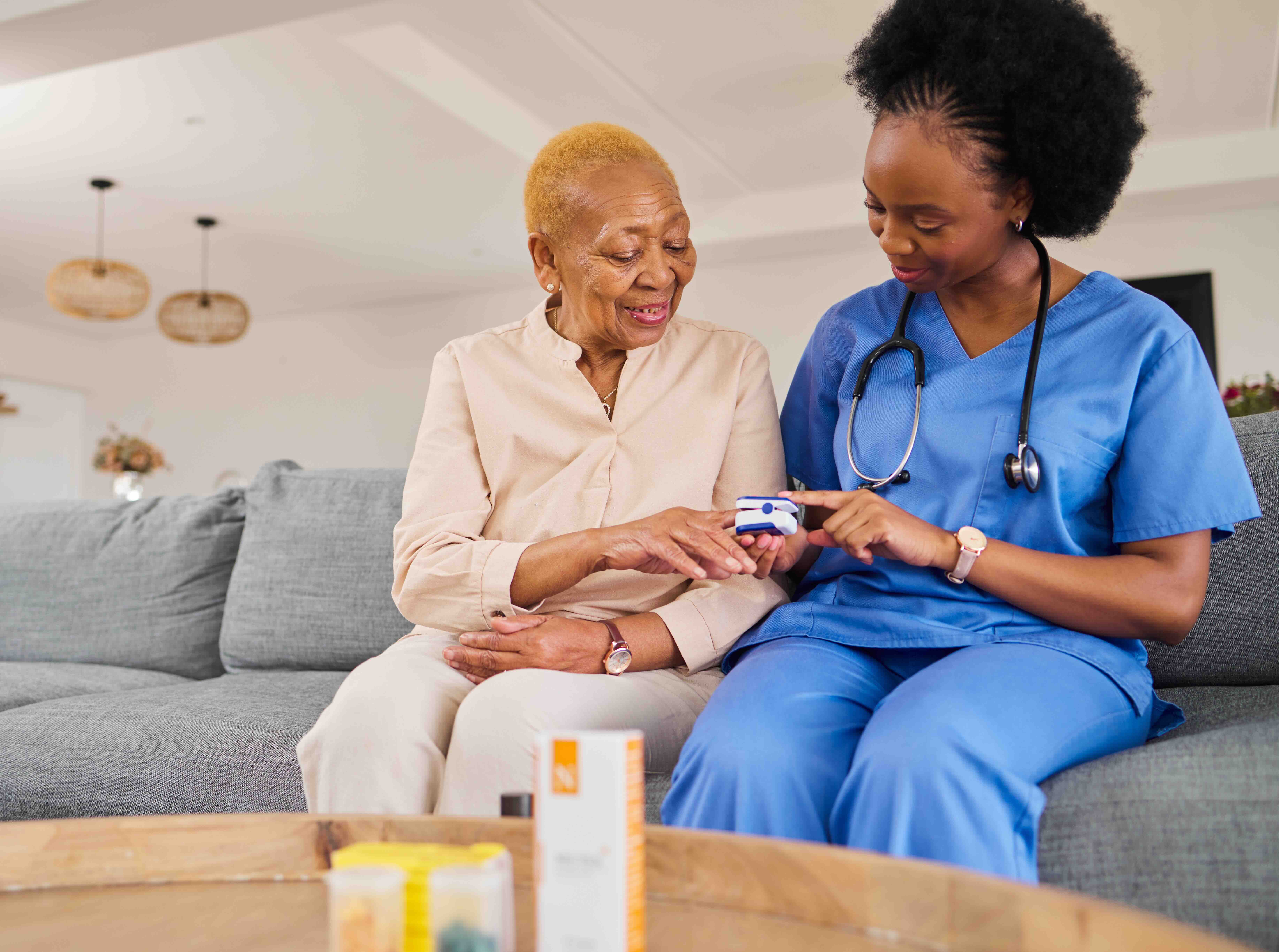 A home health nurse provides coordinated care by helping an older adult use a pulse oximeter during an in-home visit, supporting communication and safety.