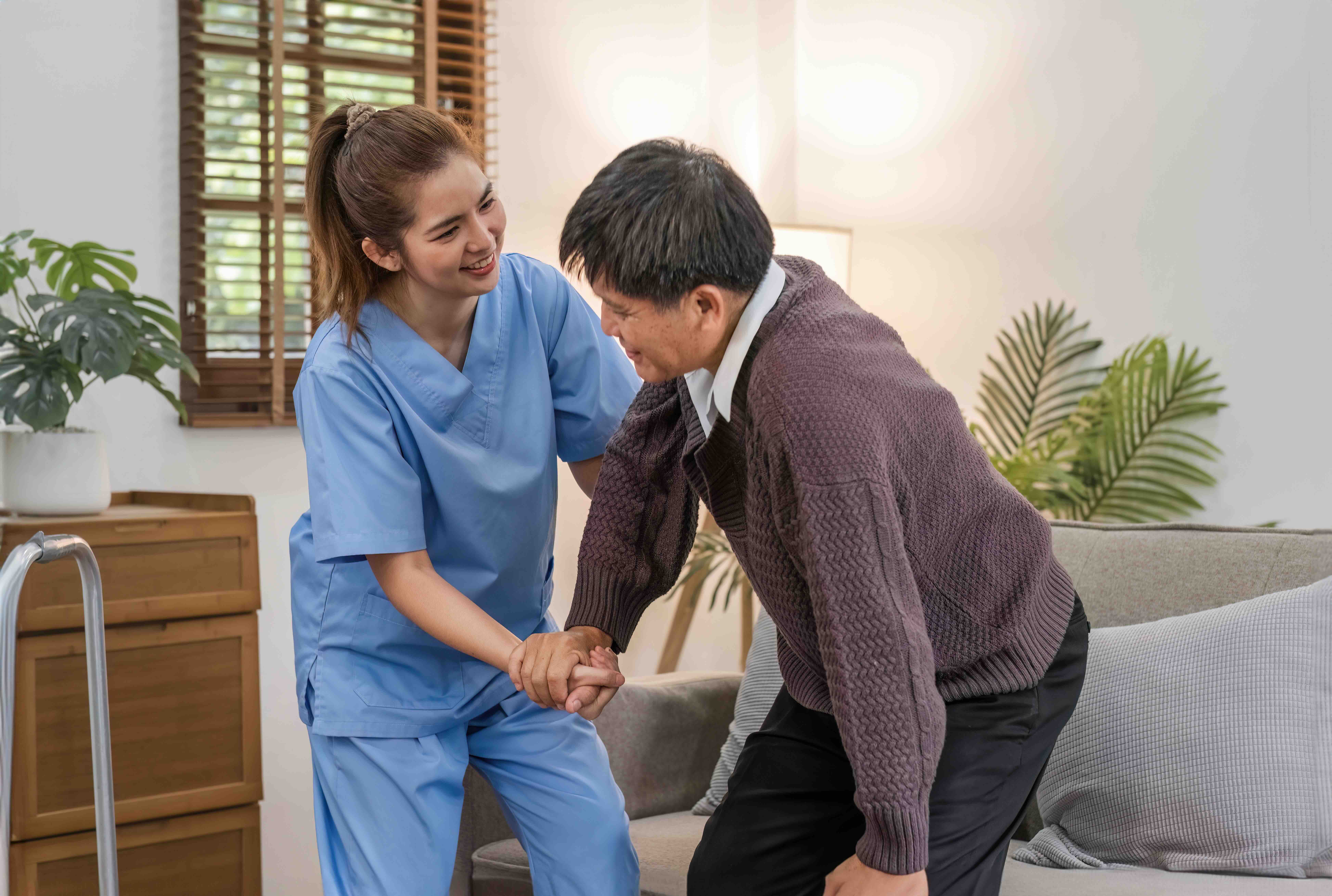 A caregiver from a home health care agency assists an older adult as they stand, demonstrating supportive coordinated care and safe mobility at home.