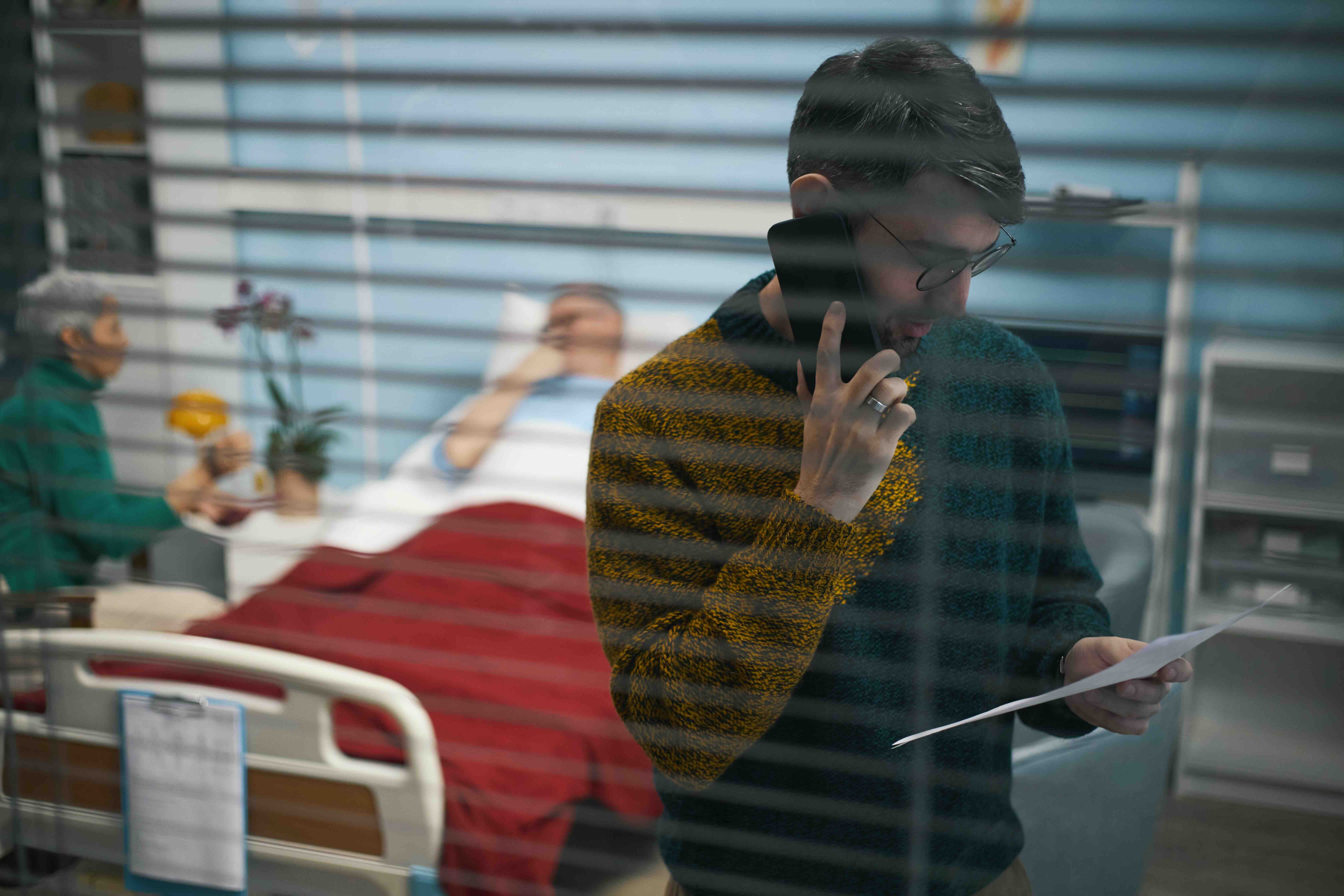 Caregiver on the phone reviewing medical paperwork during a family emergency, preparing documents for a hospital visit and organizing records through secure digital document management rather than relying only on an emergency kit.