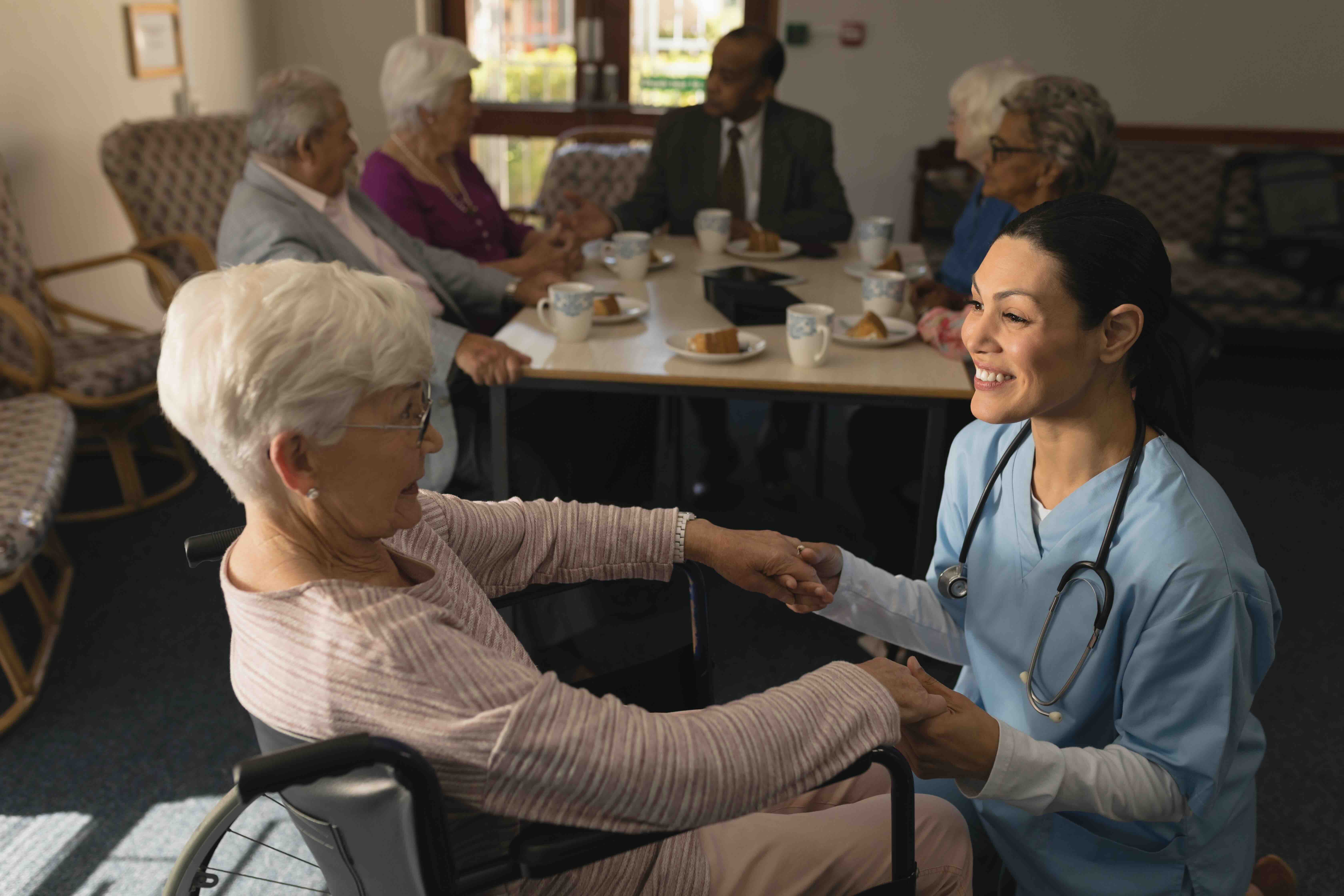 Caregiver holding hands with an elderly woman in a wheelchair inside a medicaid nursing home, highlighting compassionate long-term care