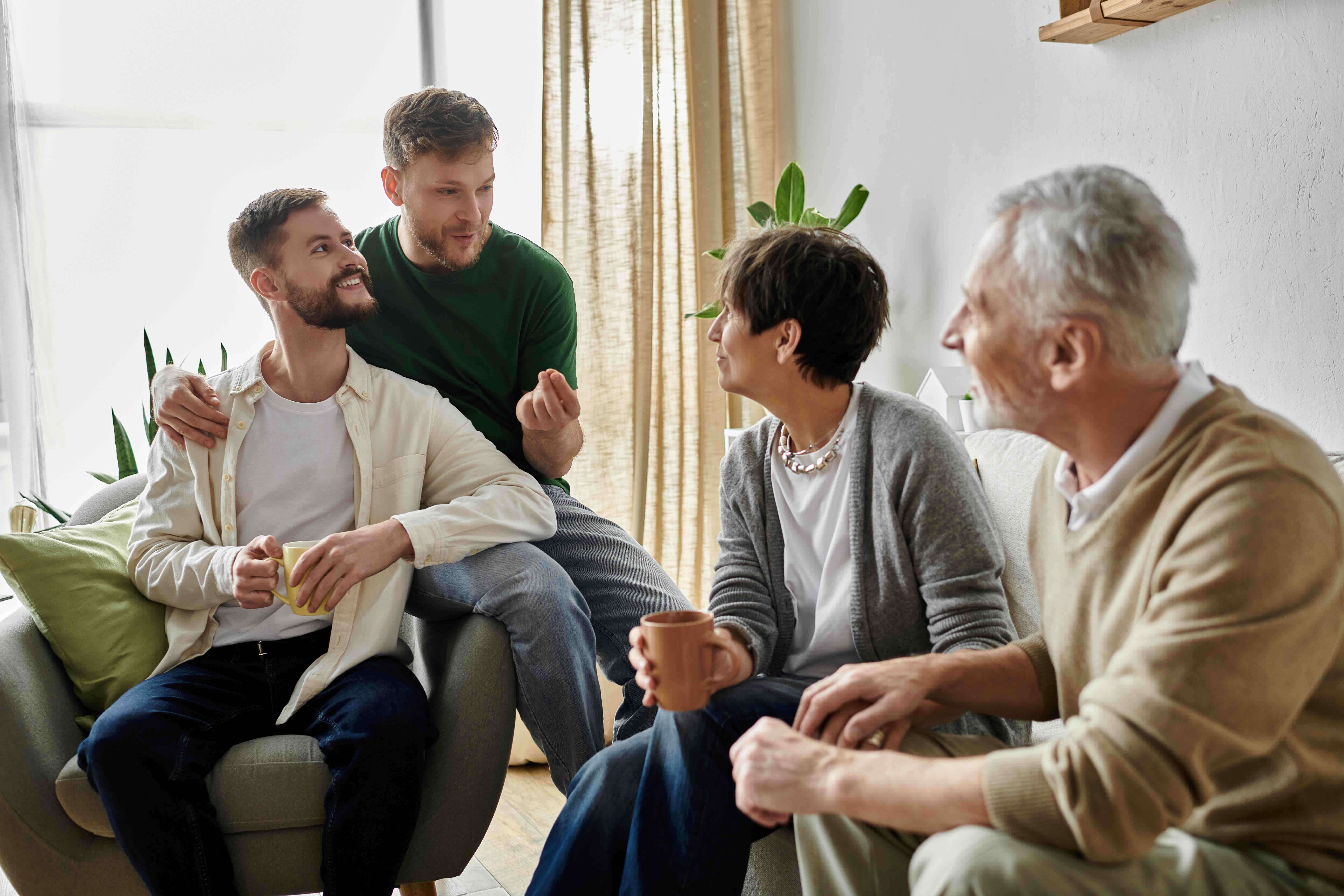 Family members sit together in a living room, talking and holding mugs during a care planning conversation, reflecting coordinated care and shared communication among loved ones supporting an older adult.