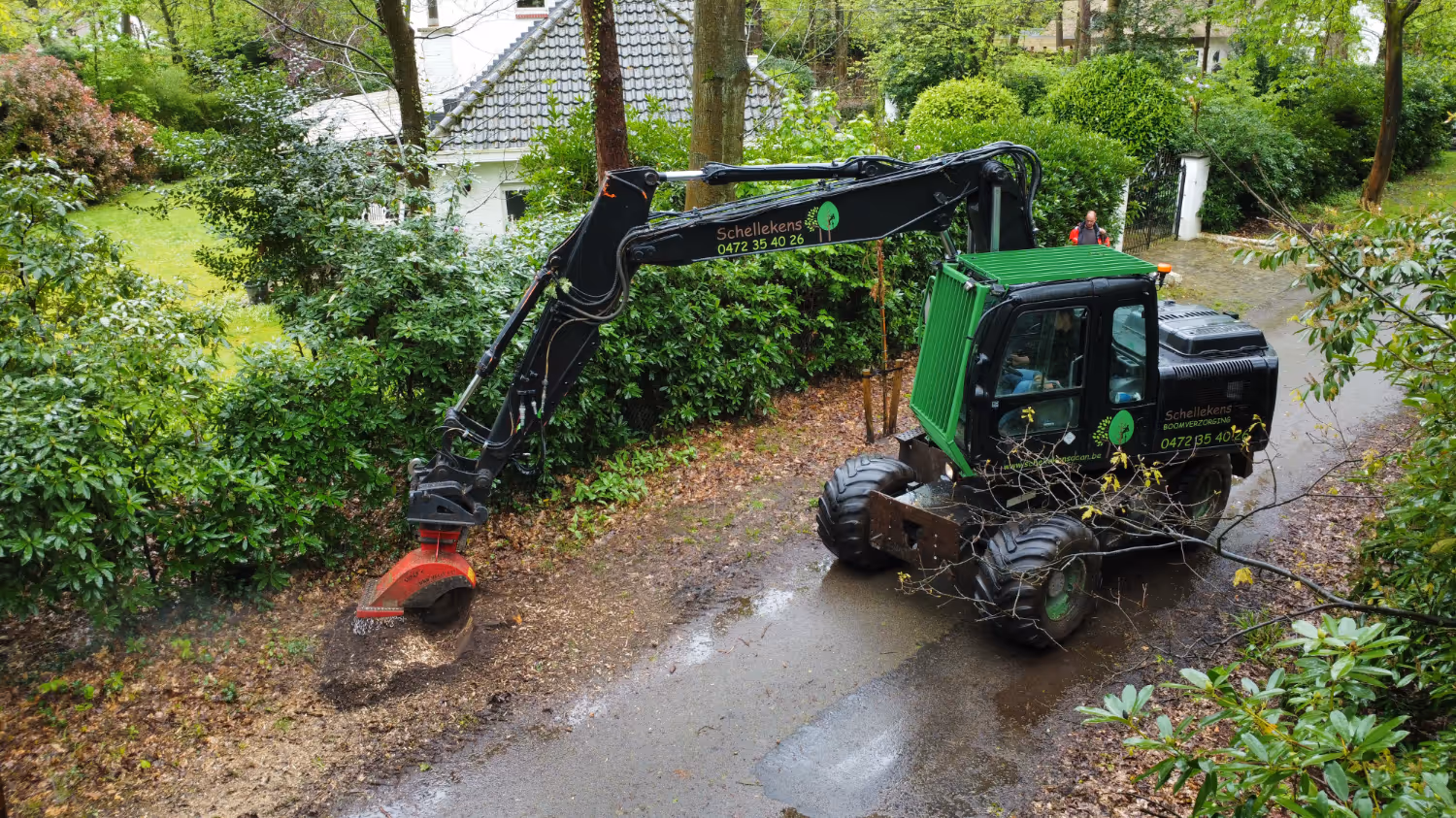 Een groene graafmachine met grote wielen vermaalt een boomstronk op een onverhard pad. Omringd door weelderig groen straalt de machine efficiëntie en focus uit.