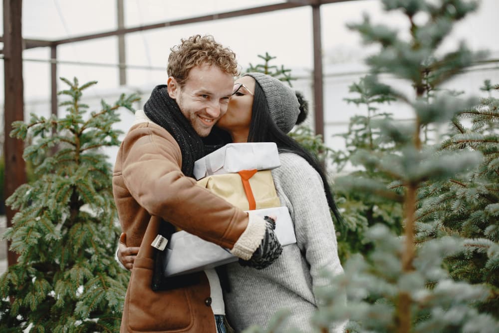 Couple heureux s’enlaçant avec des cadeaux, illustrant la joie et la chaleur d’une attention sincère.