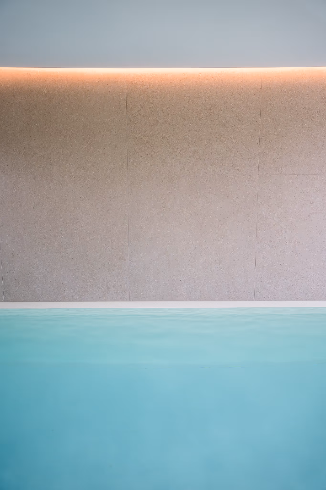 Minimalistischer Innenpool mit türkisfarbenem Wasser, beiger Wand und warmem Lichtstreifen oben.