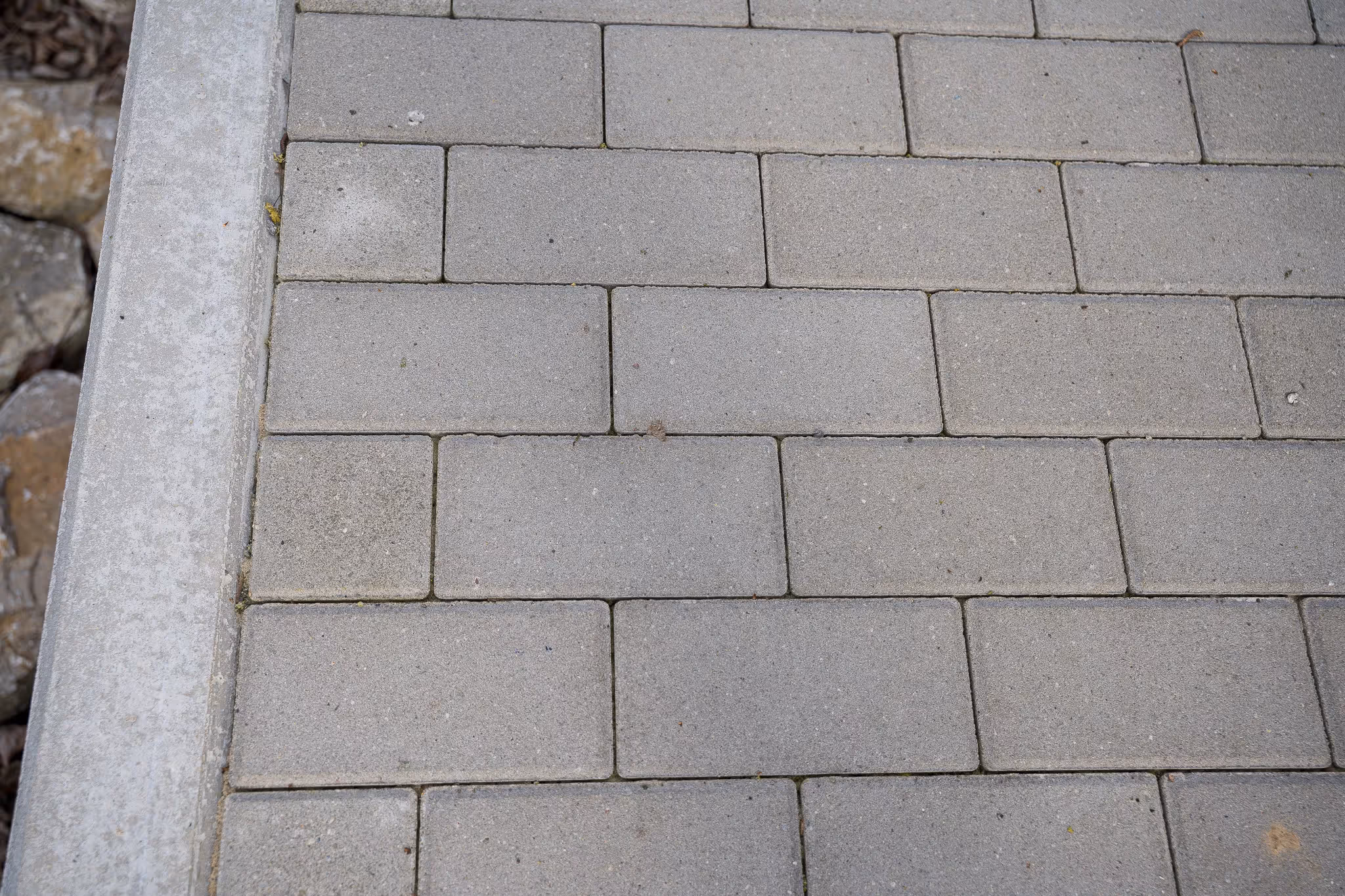 Grau gepflasterter Gehweg mit Betonbordstein und Steinen links.