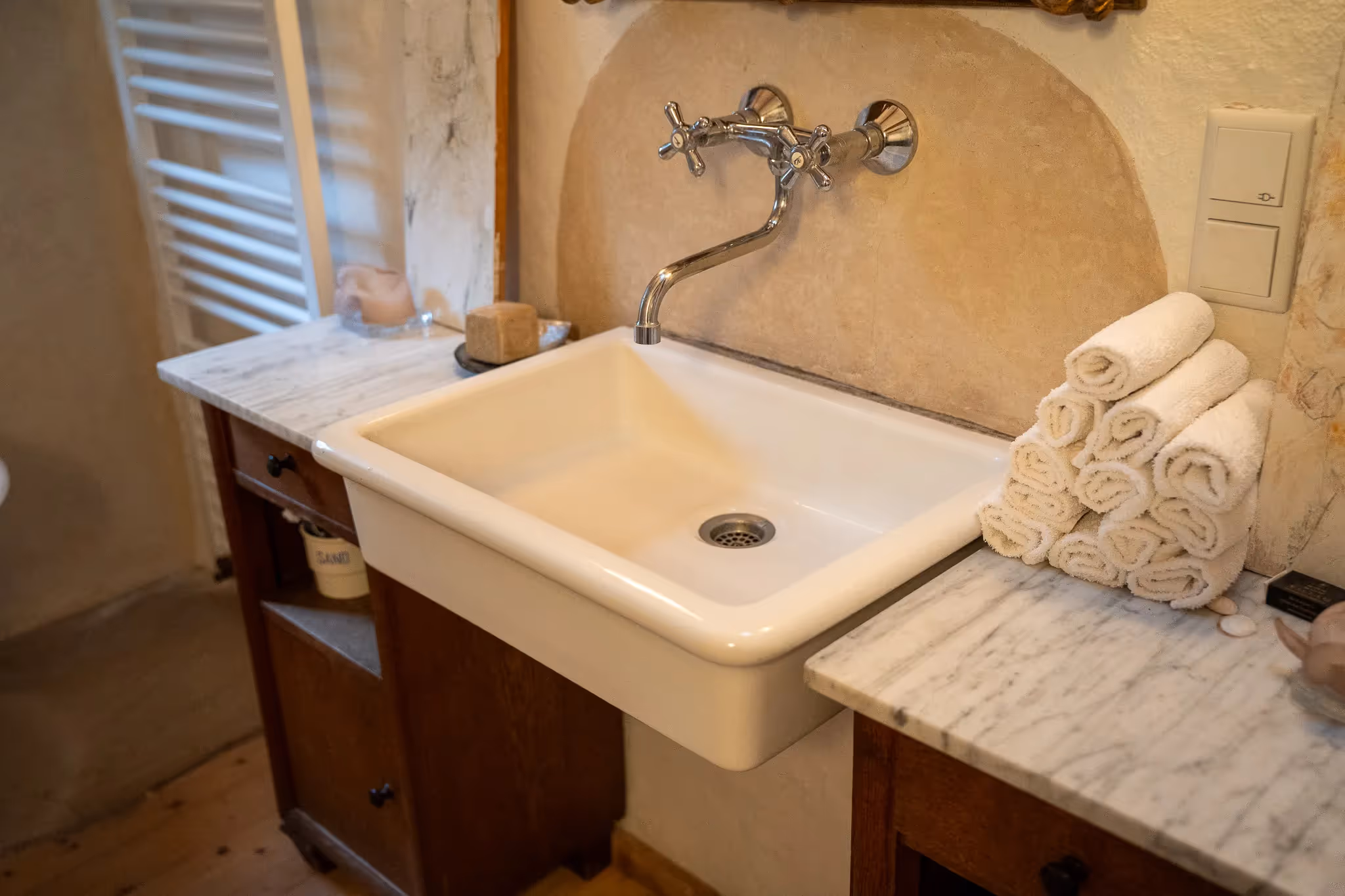 Badezimmerwaschbecken mit Wandarmatur, Marmorarbeitsplatten und einem Stapel weißer Handtücher.