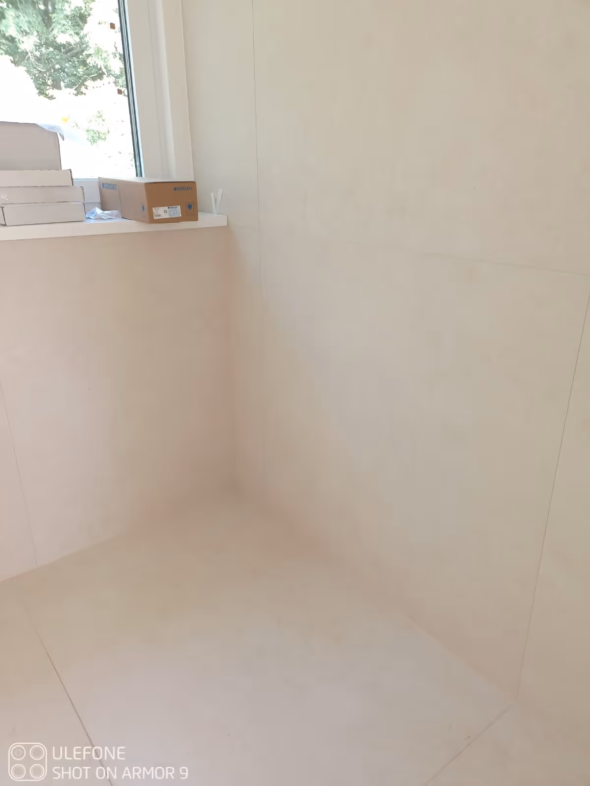 Leere weiße Fliesenecke mit einem Fenster und mehreren Kartons auf der Fensterbank.