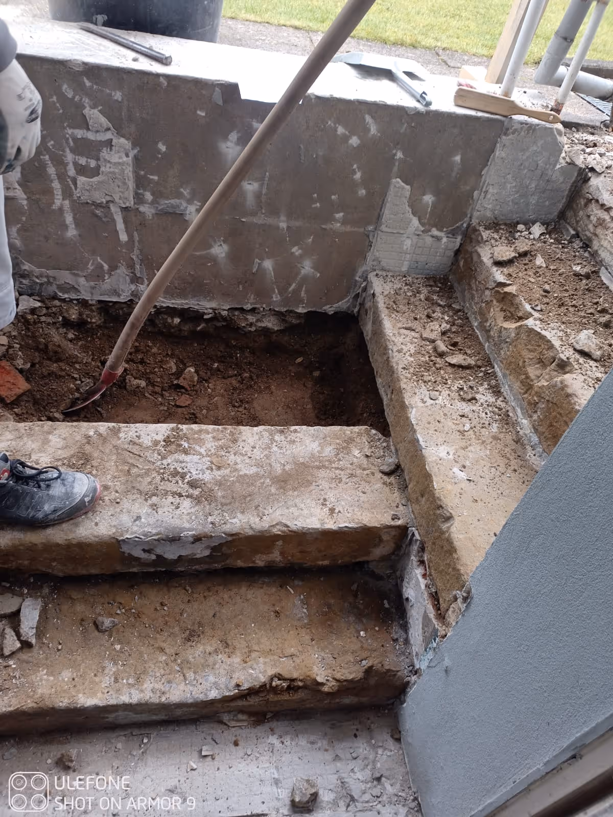 Renovierungsarbeiten an einer betonierten Außentreppe mit Schaufel und einem Arbeiter mit Handschuhen und Sicherheitsschuhen.